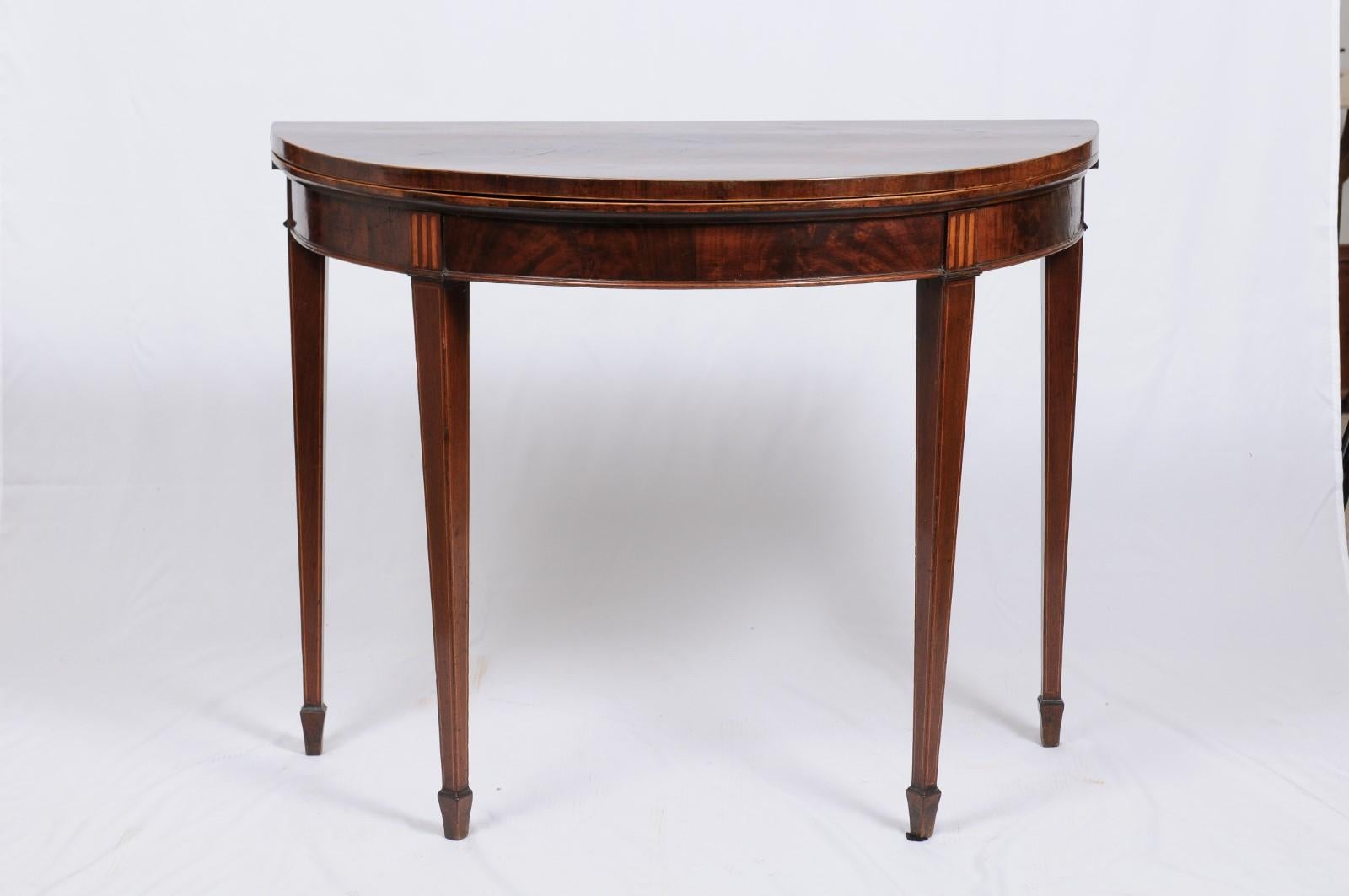 An antique inlaid Federal-style demilune table that can be used as a console table when closed or opened for use as a game or dining table. The leather top opens to reveal beautiful bookmatched veneer. Fruitwood inlay in a classical design adorns