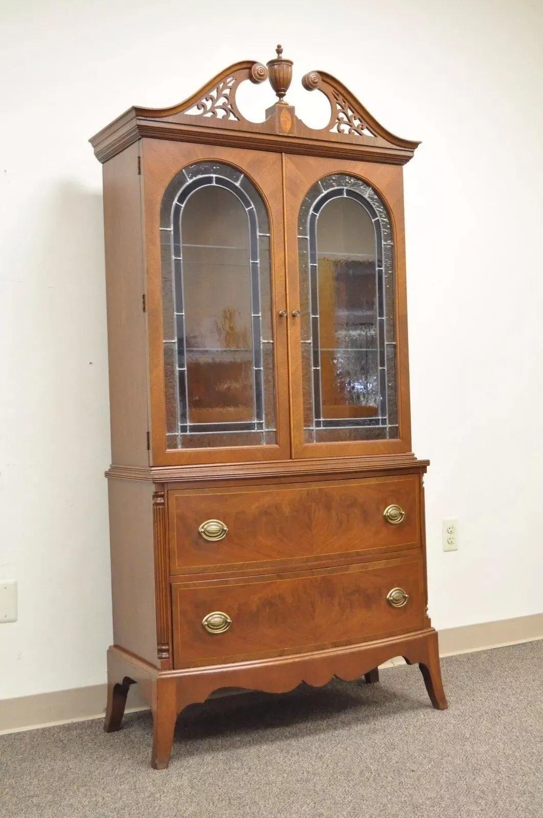 Antique Federal Style Mahogany China Display Cabinet with Stained Glass Doors. Item features a pierced carved arch, urn finial, inlaid crest, blue accented leaded and stained glass doors, 2 adjustable glass shelves, 2 dovetailed drawers with pencil