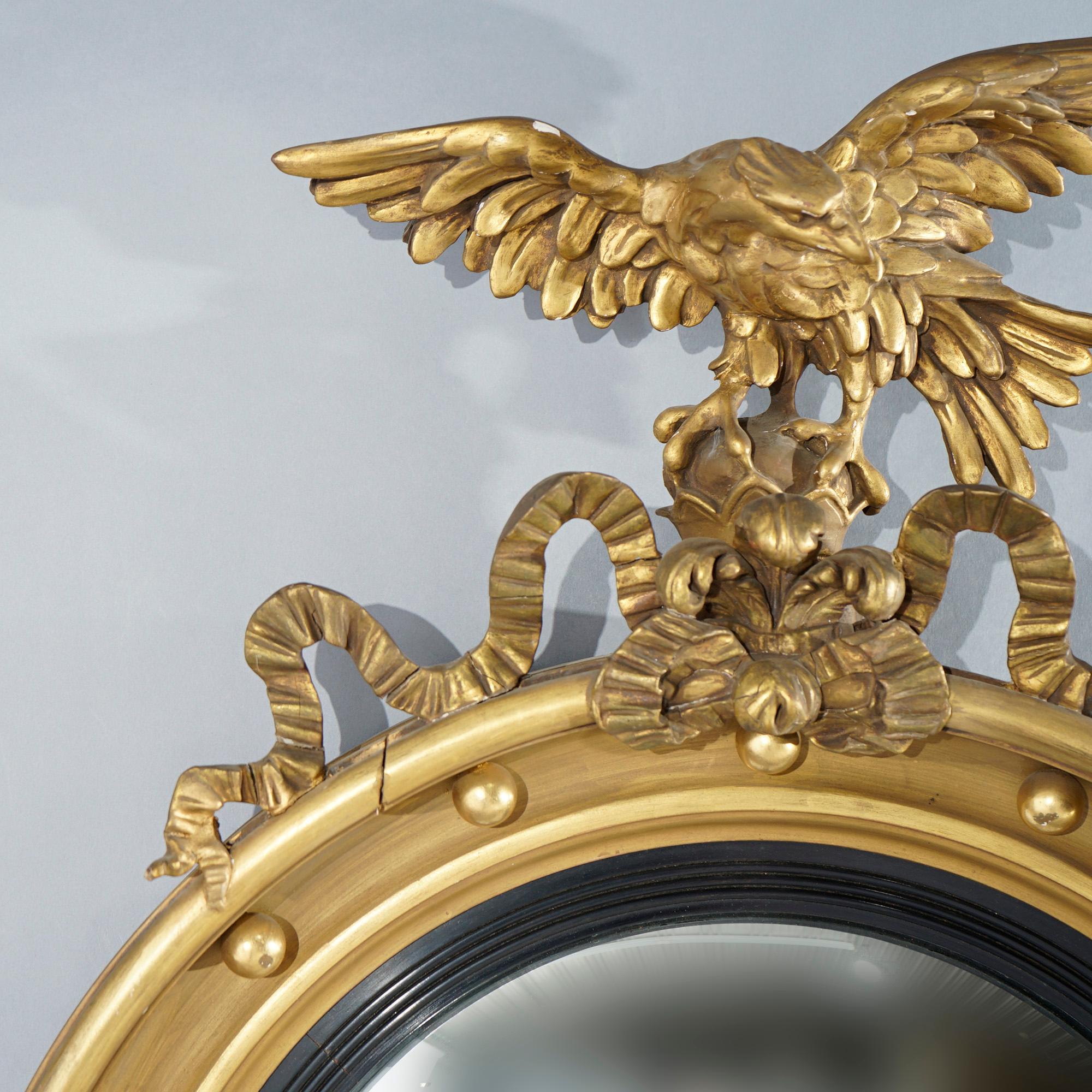 An antique Federal Revival wall mirror offers giltwood frame with figural eagle form finial, convex mirror and foliate elements, c1890

Measures - overall 39.5''H x 26''W x 5''D; sight 22'' diam.