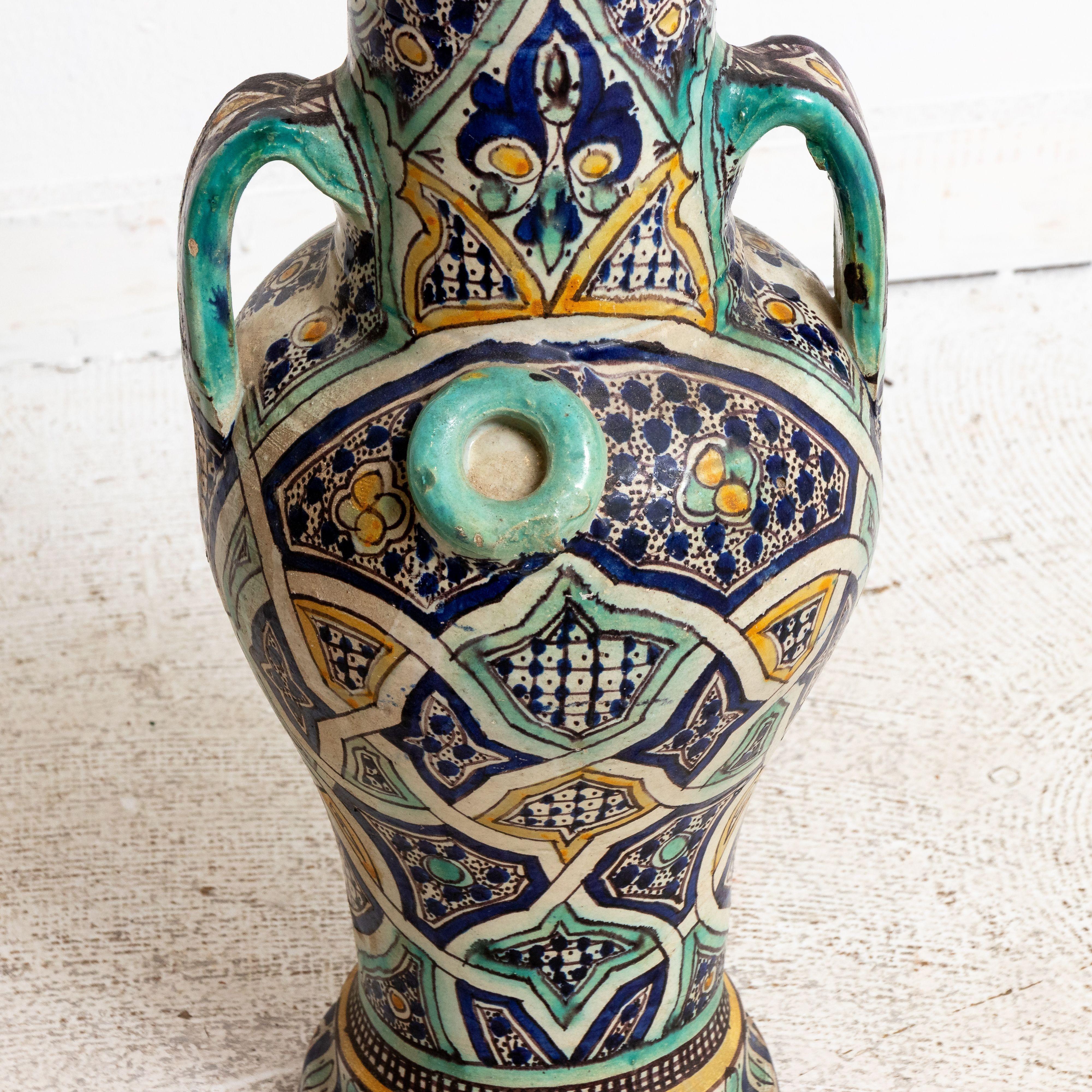 Circa early 20th century antique blue, yellow, and aqua painted ceramic fez vase with two handles. The piece is further detailed with geometric and floral designs throughout. Made in Morocco. Please note of wear consistent with age.