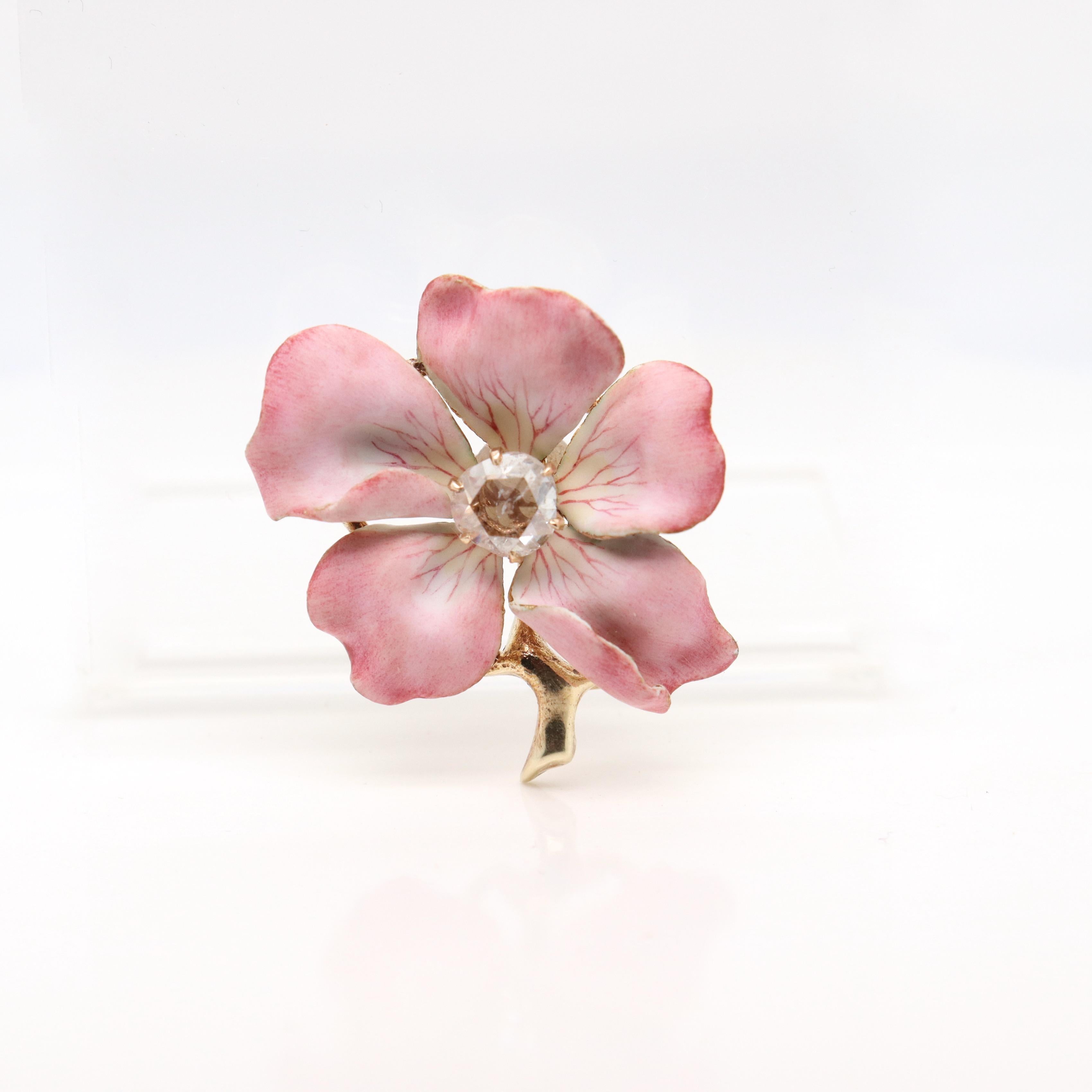 A fine antique figural flower brooch.

In the form of a 5 petal dogwood or pansy flower with pale pink & yellow petals and a gold stem.

Prong-set with an off-round rose cut diamond to the center of the flower.

Simply a wonderful