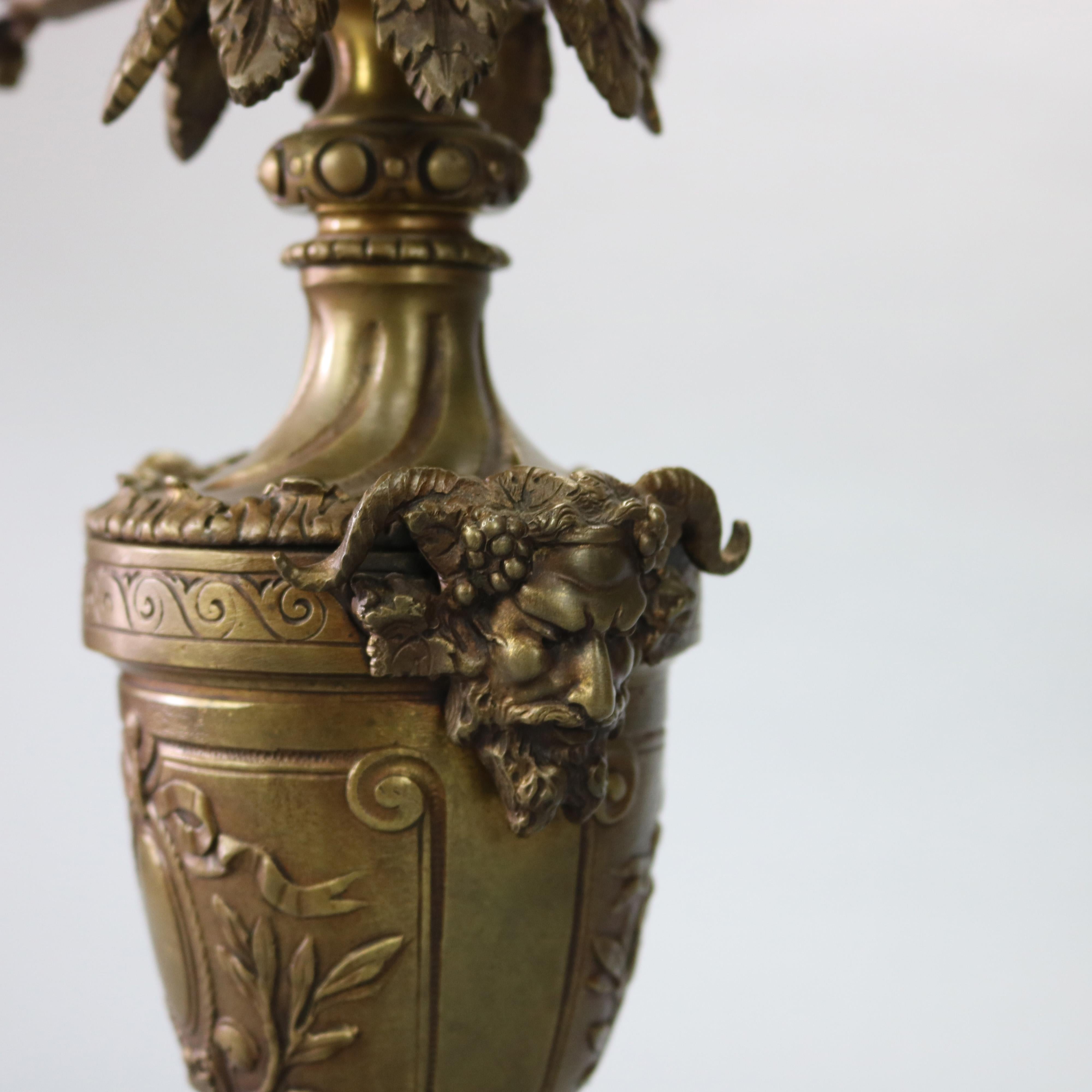 An antique figural French Rococo candelabra lamp offers cast bronze construction with urn form font having relief medallion with foliate surround, flanking satyr head handles and foliate form arms terminating in candle lights and raised on stepped