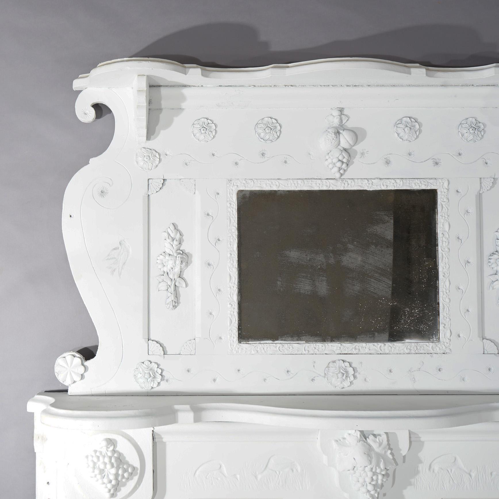 An antique architectural fireplace surround offers mirrored upper with shaped scroll form frame over surround having mantel, carved grapes in relief, marsh scenes with birds and floral elements, painted, c1890

Measures- Mirror 30.5''H x 53.5''W x