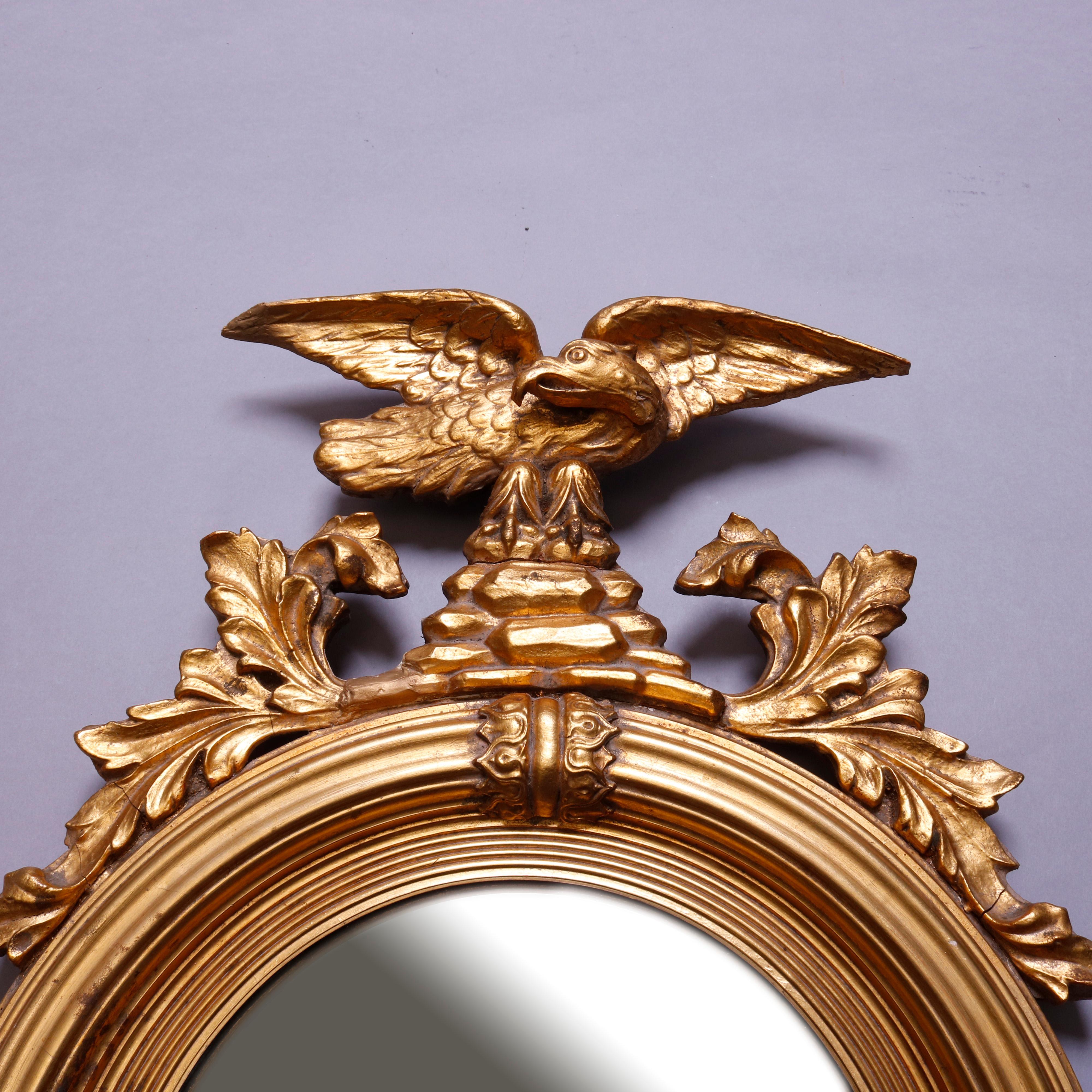 An antique figural Federal style figural giltwood wall mirror features crest with eagle flanked by acanthus surmounting round convex bullseye mirror with reeded frame having foliate decoration, 20th century

***DELIVERY NOTICE – Due to COVID-19 we