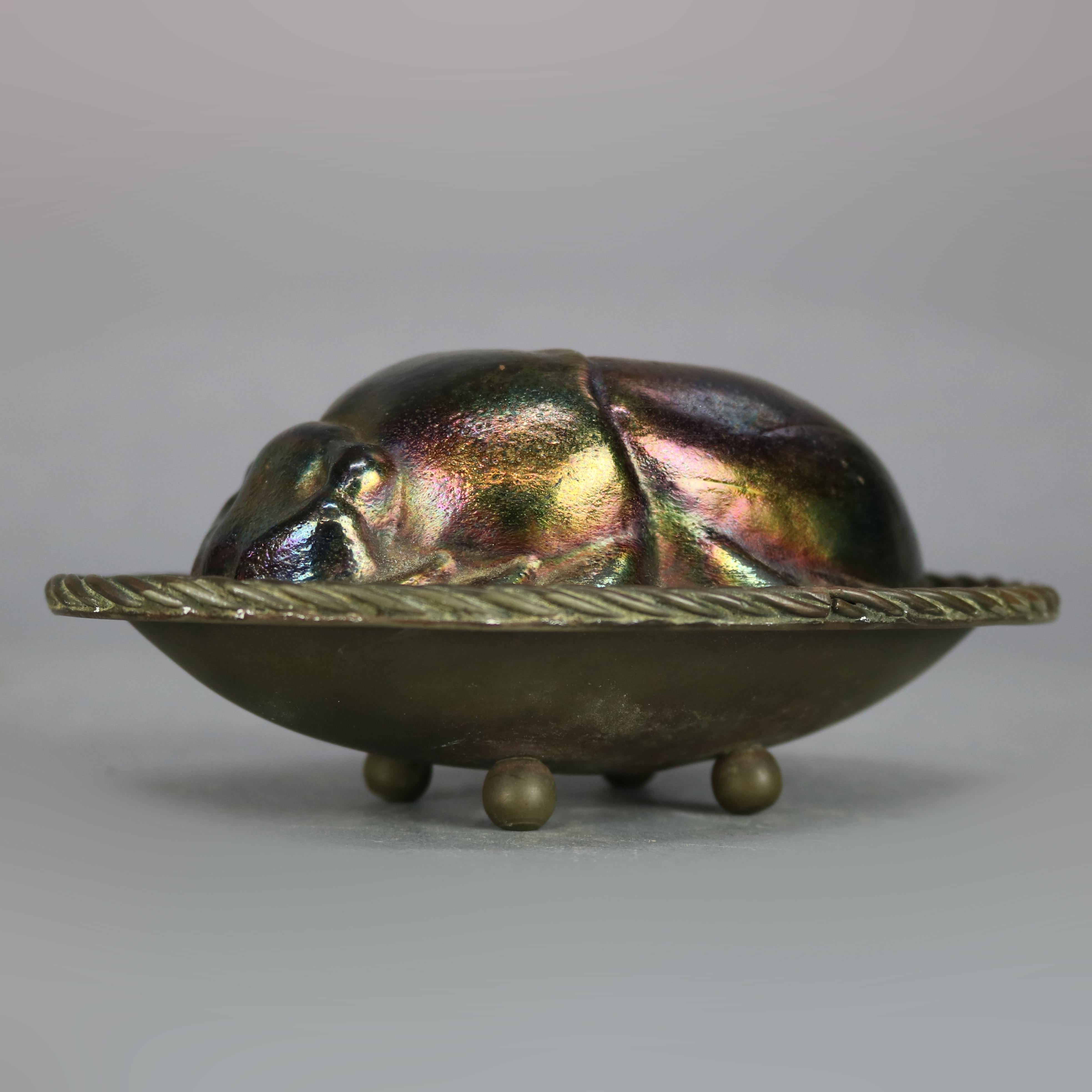 An antique figural sculpture in the manner of Tiffany Studios offers art glass in the form of a scarab (beetle) seated on cast bronze tray having gadroon edge and seated on ball feet, later added stamp on base 