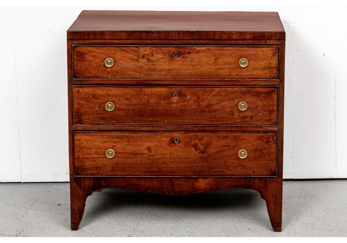 An authentic and handsome three drawer Bachelor's Chest dating to the 19th Century. The top with black string inlaid edges. Three graduated long drawers with carved moldings, brass key holes (lacking a key) and fine leafy brass ring pulls. The top