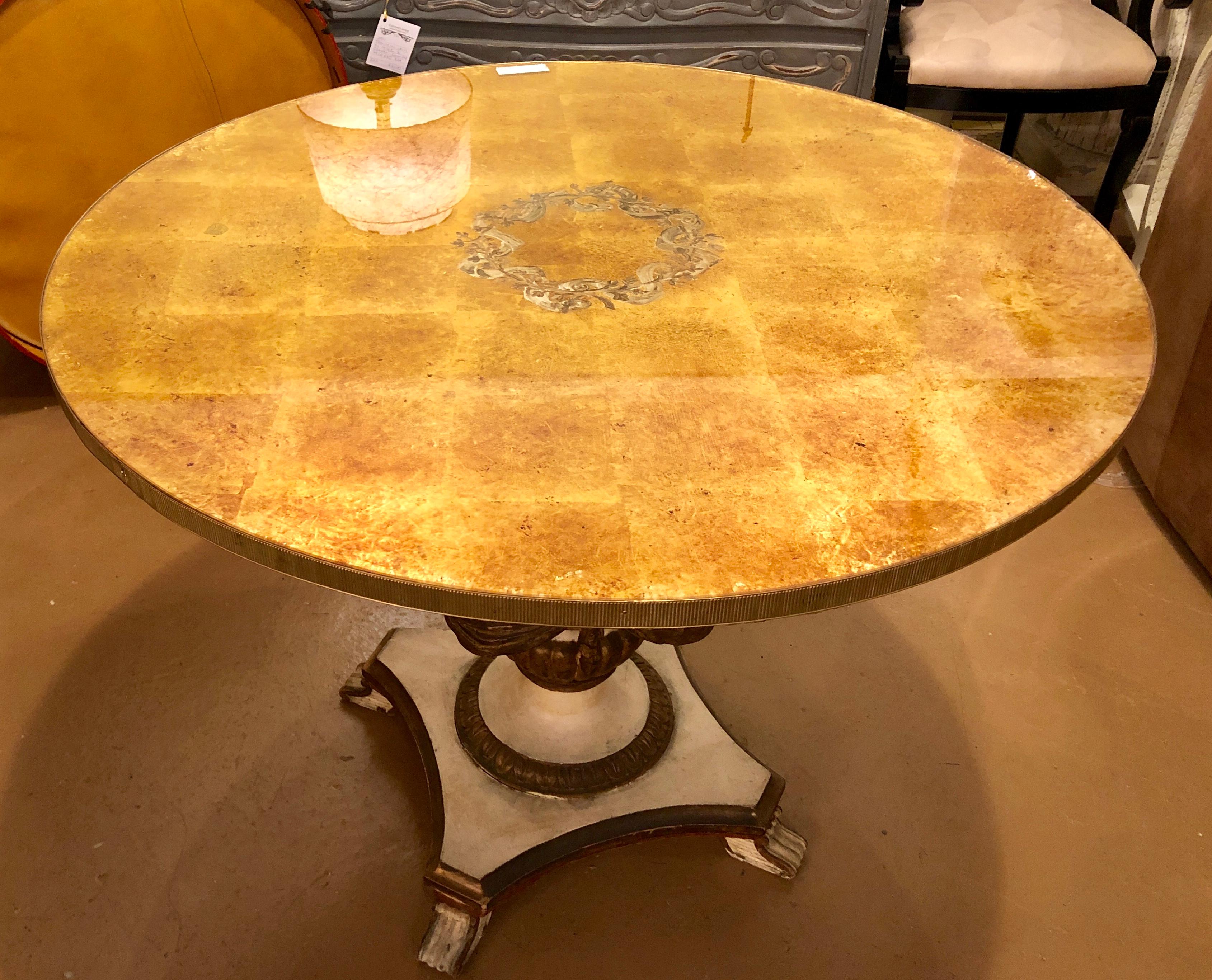 A finely decorated continental center or dining table. The gilt gold and white distressed paint decorated base with tassel and ribbon form carvings supporting a Fine Verne églomisé glass top. The top set with a bronze ribbon border.