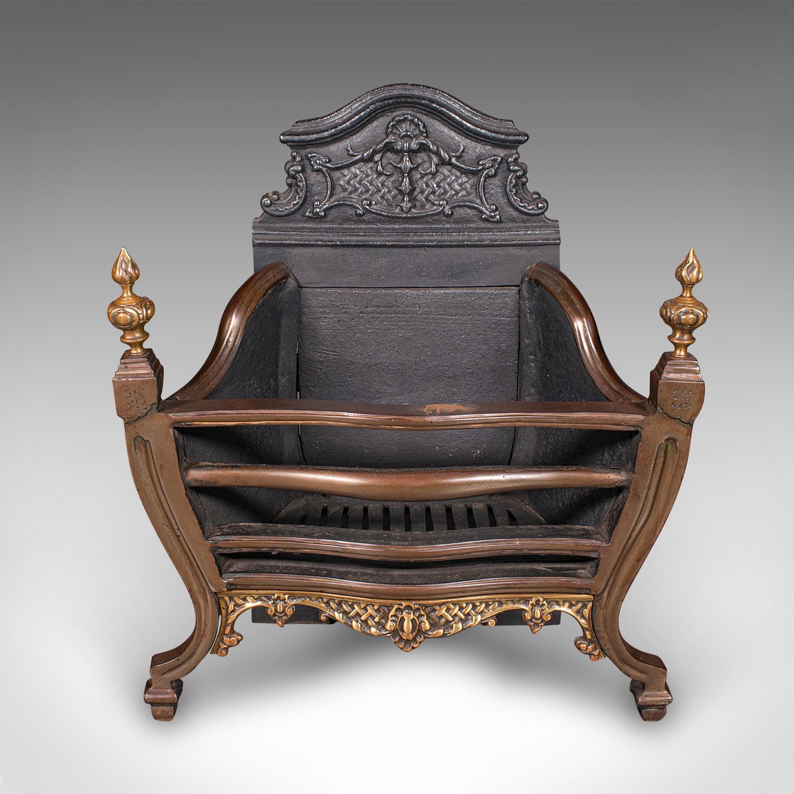 This is a delightful antique fire basket. An English, cast iron, steel and brass self-contained hearth in Georgian revival taste, dating to the late Victorian period, circa 1900. A fine example of period craftsmanship, it presents a balanced form,