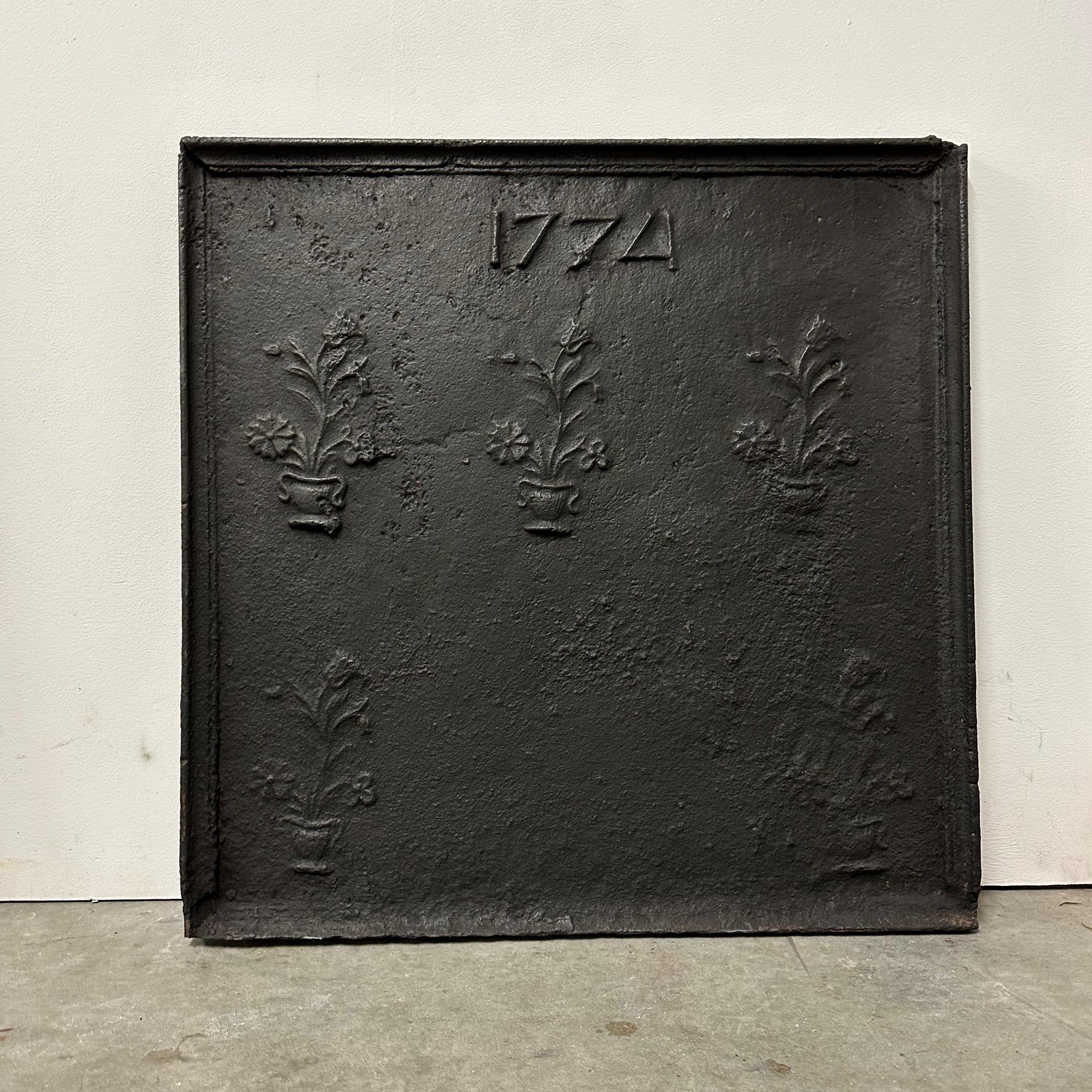 Amazing antique cast iron fireback / Beacksplash
This square beauty shows the year 1774 with 5 flowers in pots below the date.

Very unique and decorative piece.