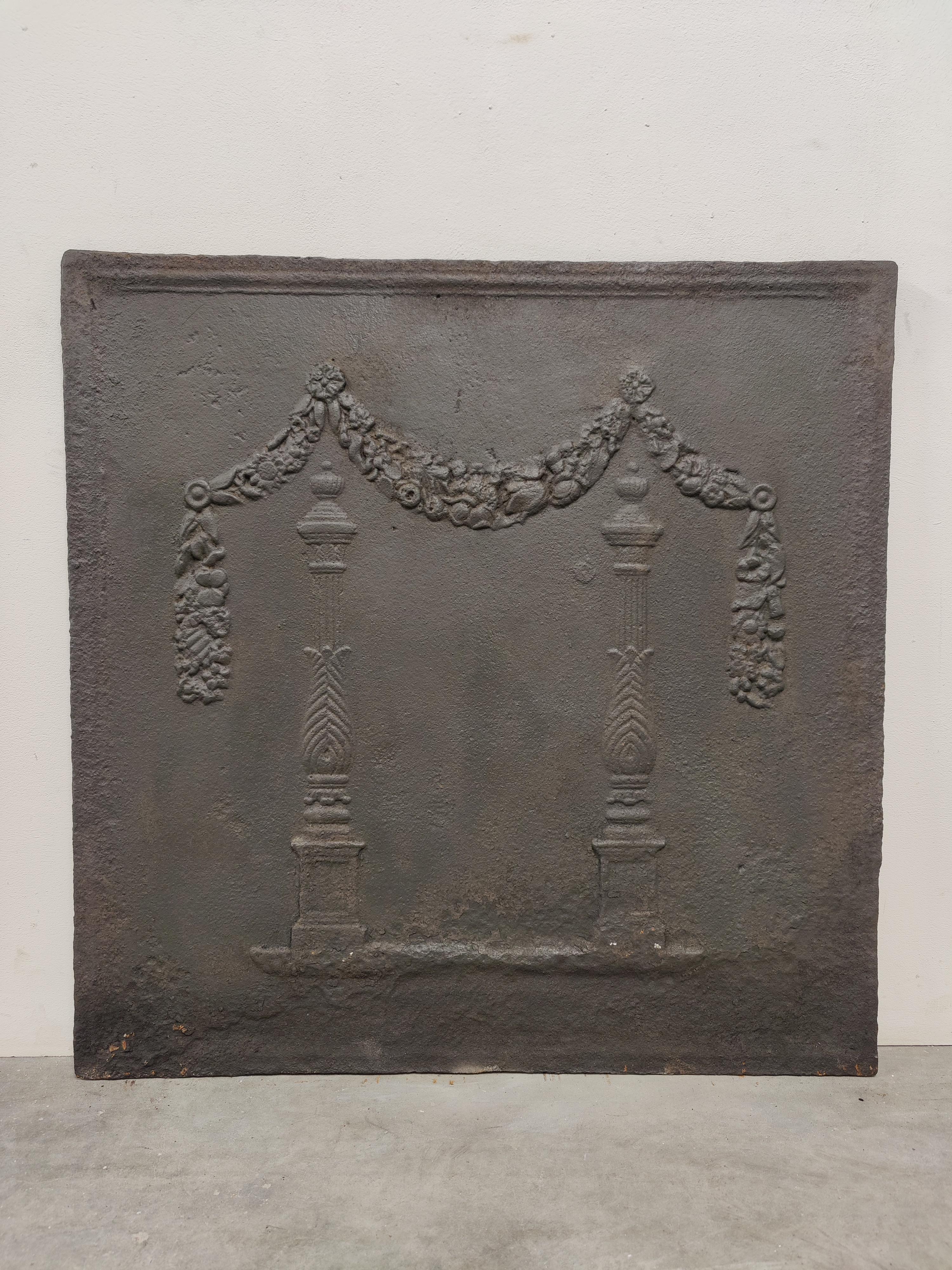 Antique fireback / backsplash, two pillars Beneath Draped Laurel Wreath.

A big and lovely square cast iron antique fireback displaying two pillars covered by laurel wreaths.
Great condition, can be used in a real gas or log fire.
Very