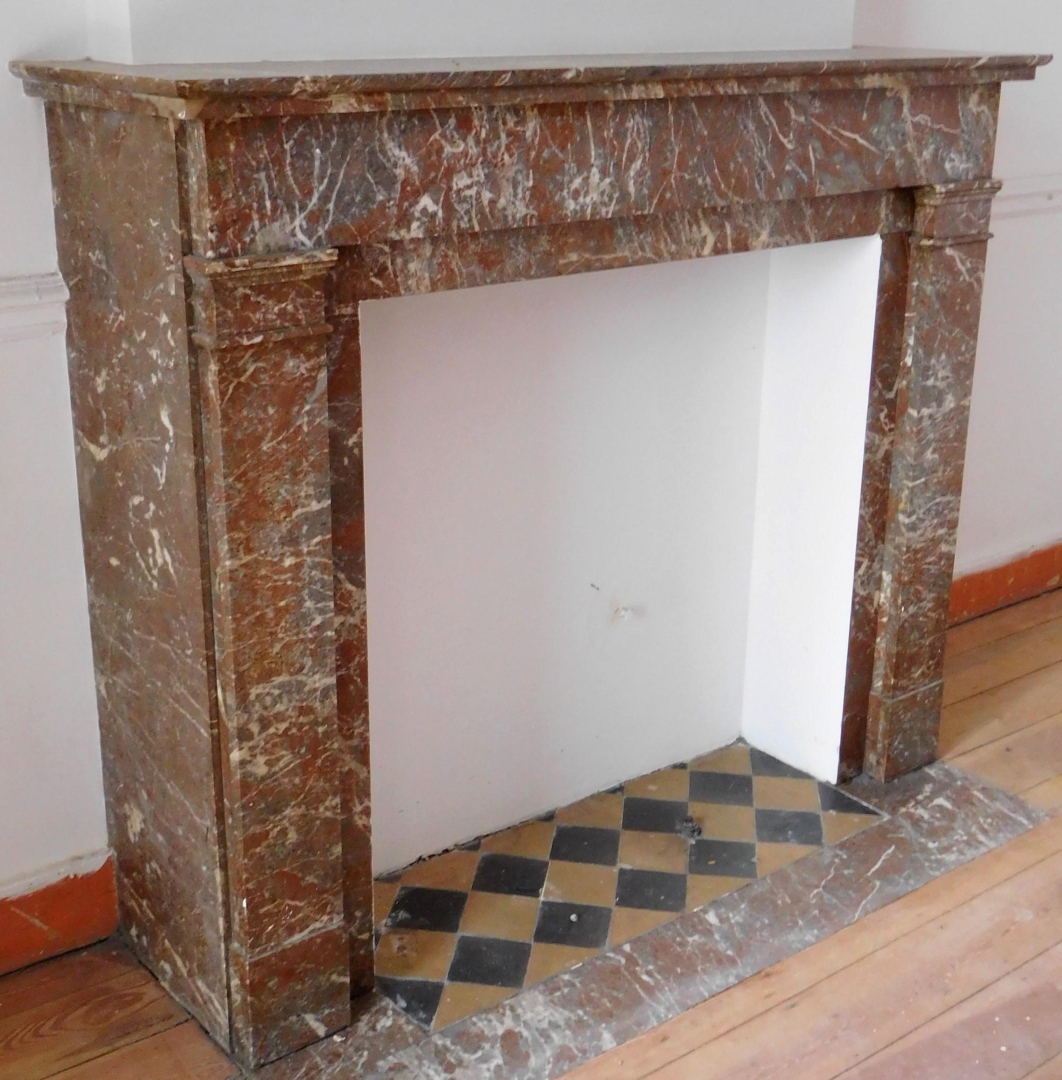 This beautiful antique fireplace in a Belgian Red marble was made in the Art Déco period. The sleek lines of this fireplace provides a subdued, quiet ambiance. The powerful color of the marble is sufficient to be impressive.  The 'Art Deco Bronze'
