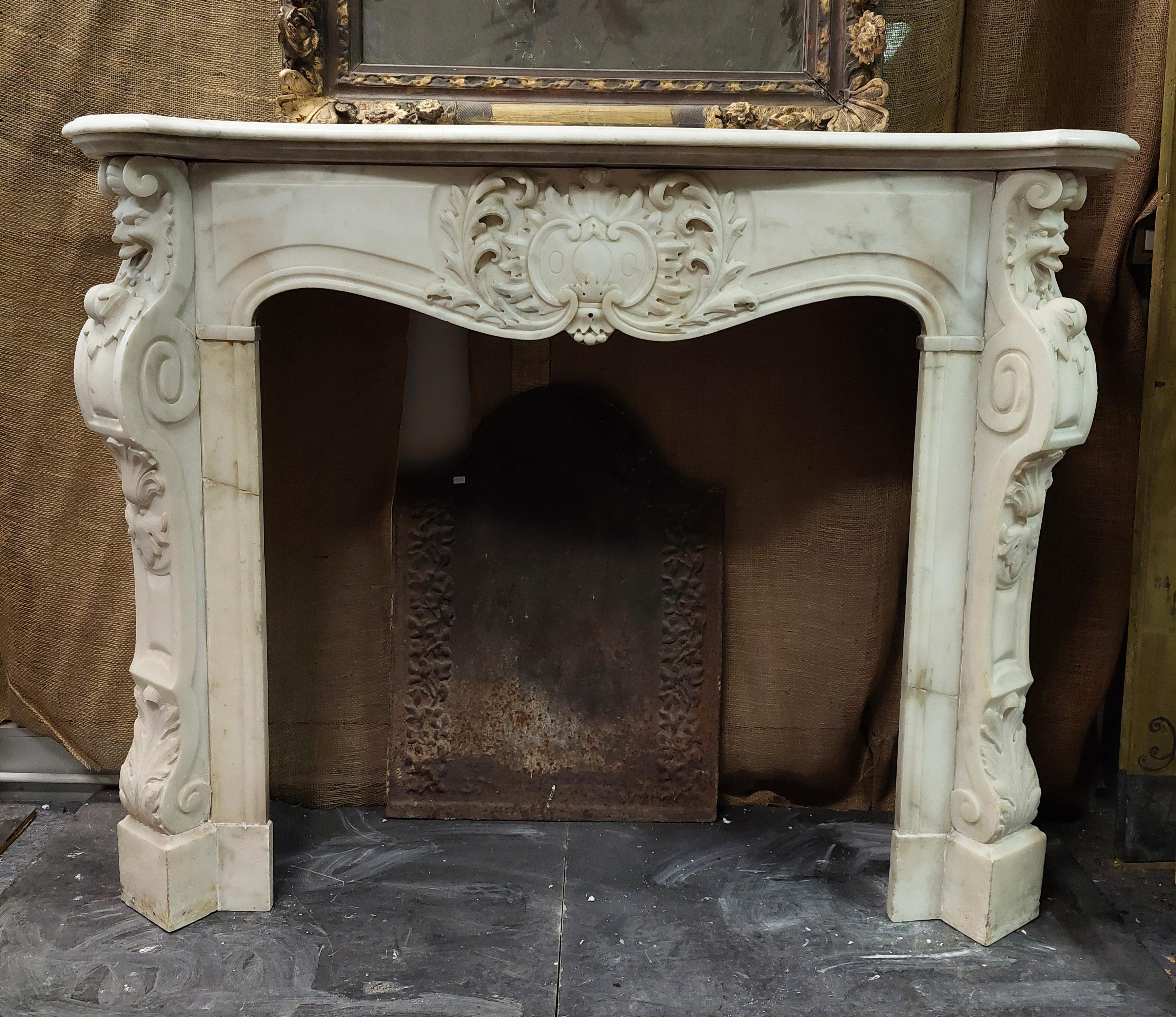 Antique fireplace mantle in white Carrara marble, richly carved both in the central shell, and in the legs and on the pediment, with many frills and masks on the sides, also carved the feet, fireplace full of charm and elegance, of great artistic
