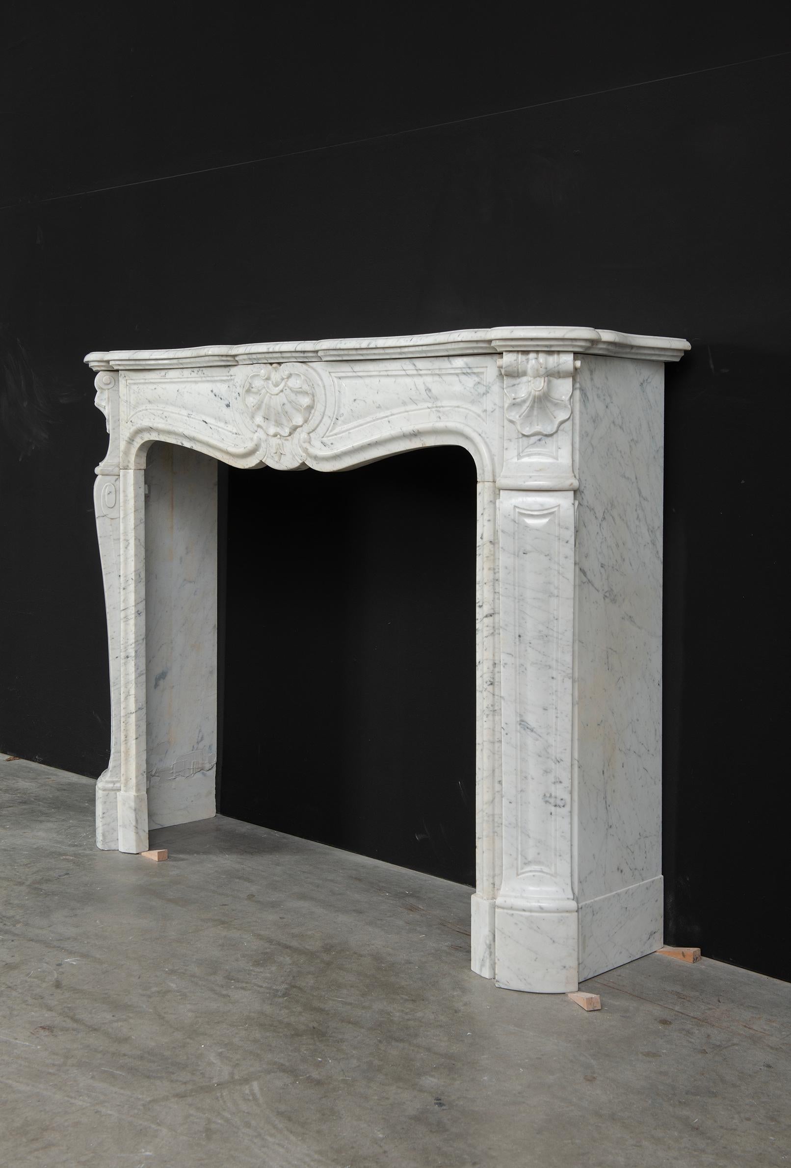 Antique Louis XV fireplace mantel in Carrara white marble from the 19th century.
Beautiful decorative piece, nice proportioned.

The serpentine breakfront shelf above a fielded freeze centered by a central shell echoed by shell decorated endblocks