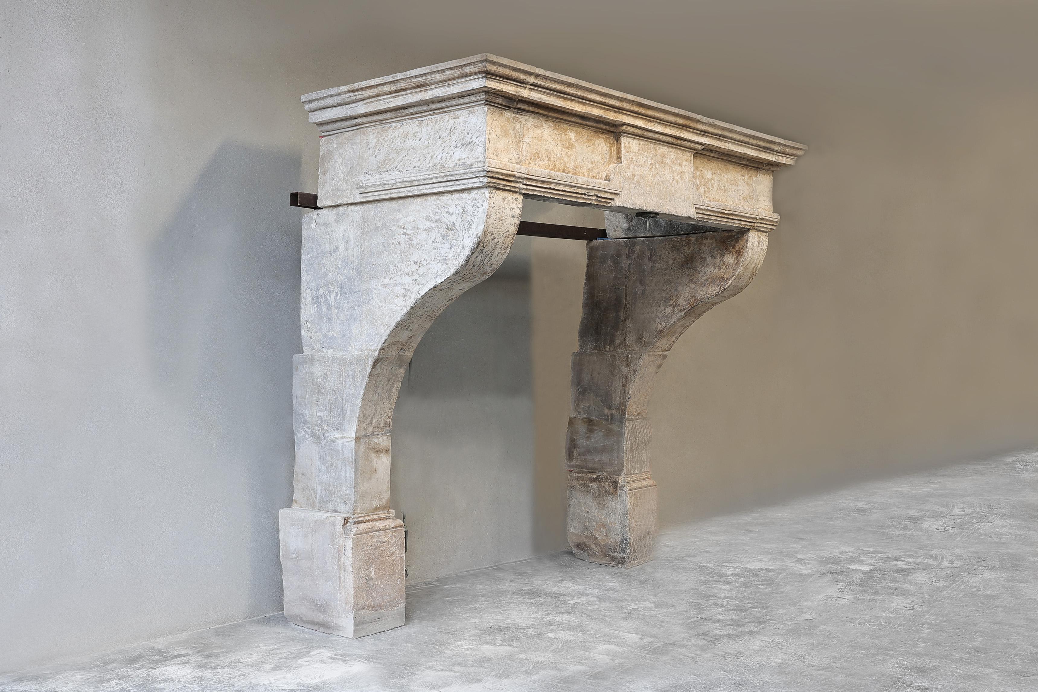Beautiful robust antique mantelpiece made of French limestone from the 18th century in the style of Louis XIII. This antique French fireplace has a beautiful wide front section and curved legs and a high base. The warm color and appearance of this