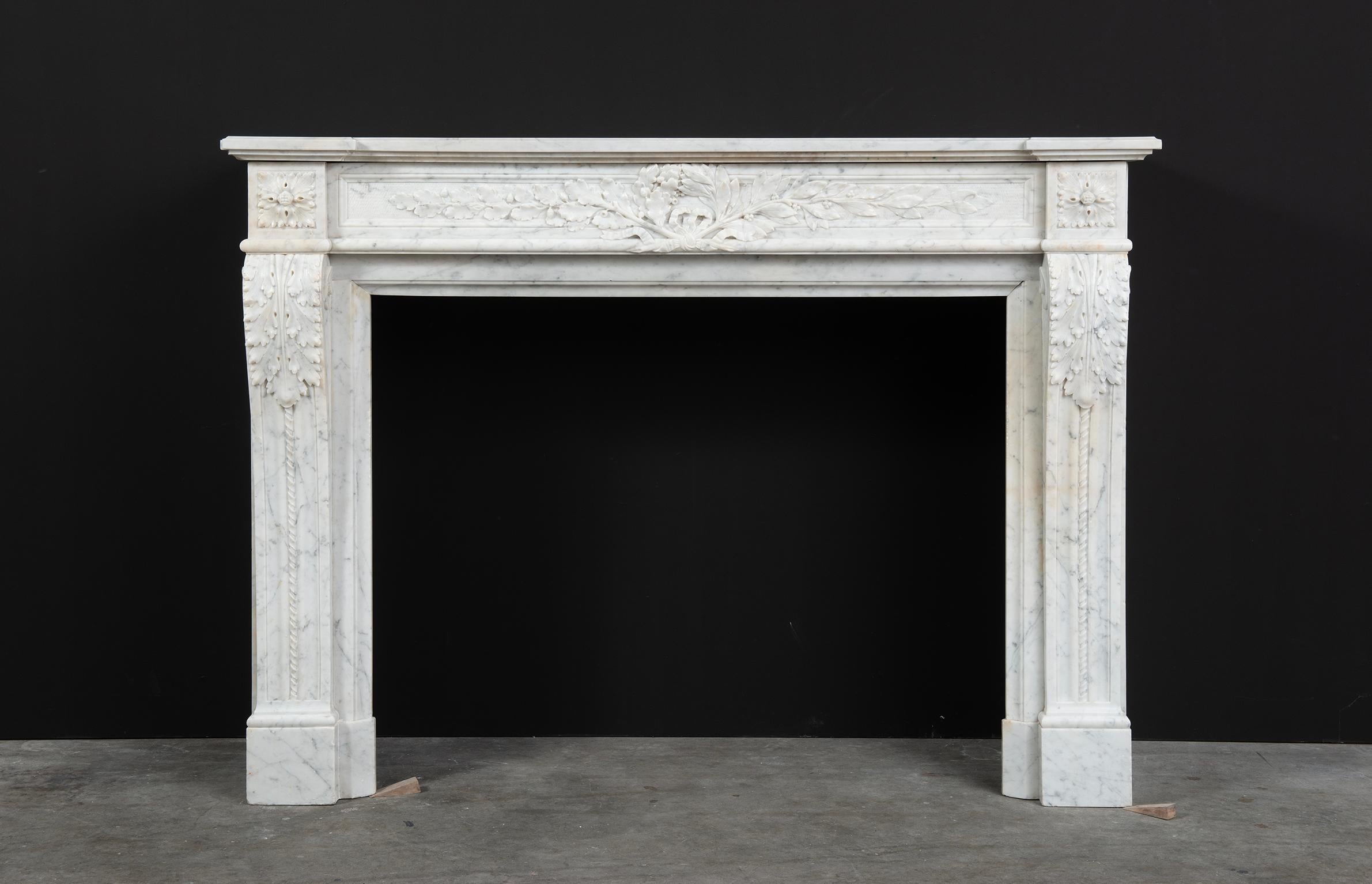 French antique Louis XVI fireplace mantel in white Carrara marble.

Strong and well profiled stepped topshelf above a finely carved paneled frieze with beautiful laurel leaves flanked by floral paterae. The scrolled jambes with paneled sides are