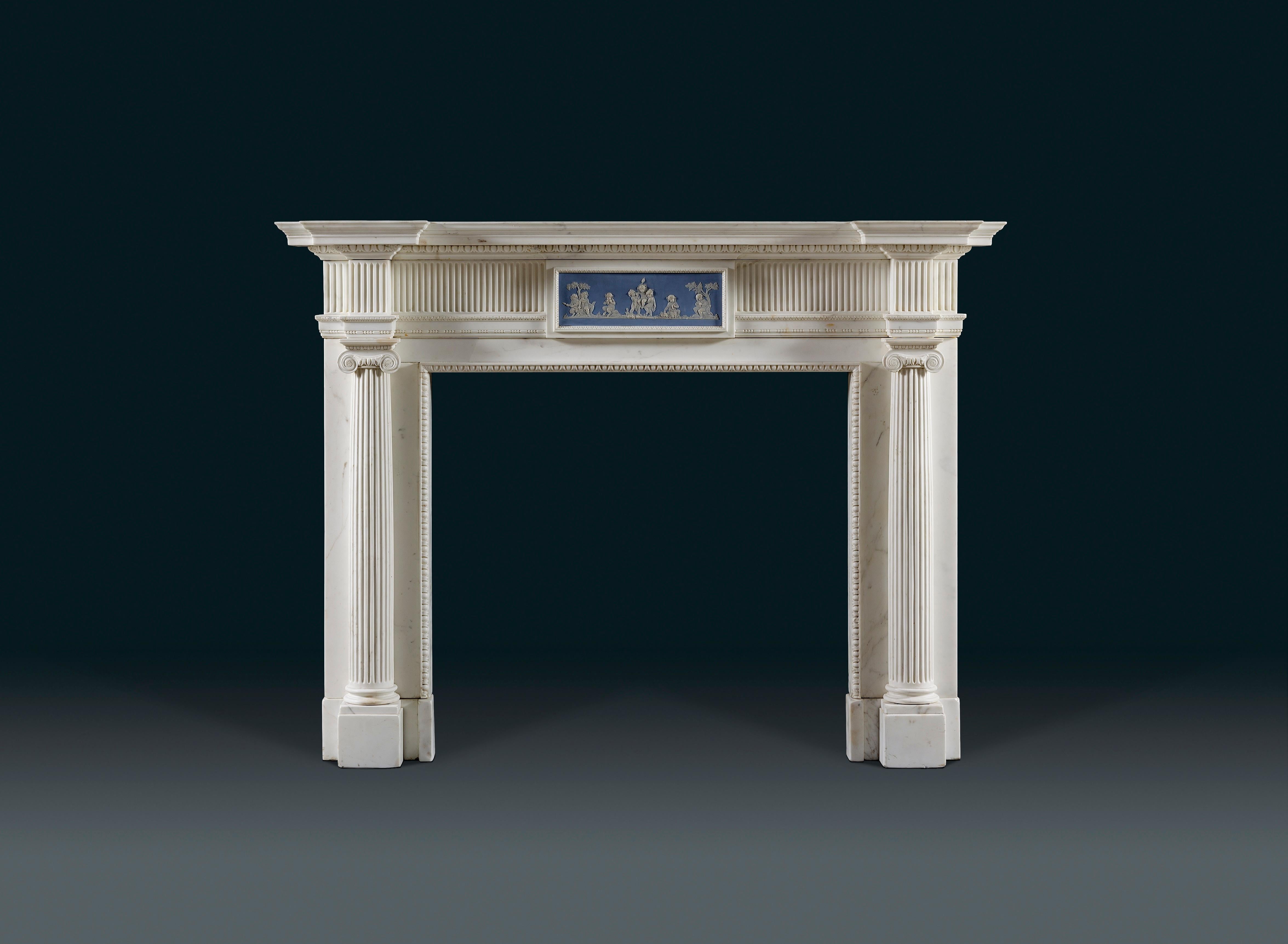 A late 18th century, early 19th century neoclassical chimneypiece in white statuary marble, centred with a Wedgwood ' Bacchanal' tablet, with 3/4 round fluted Ionic columns fronting the jambs. The Wedgwood tablet depicts a central group of three