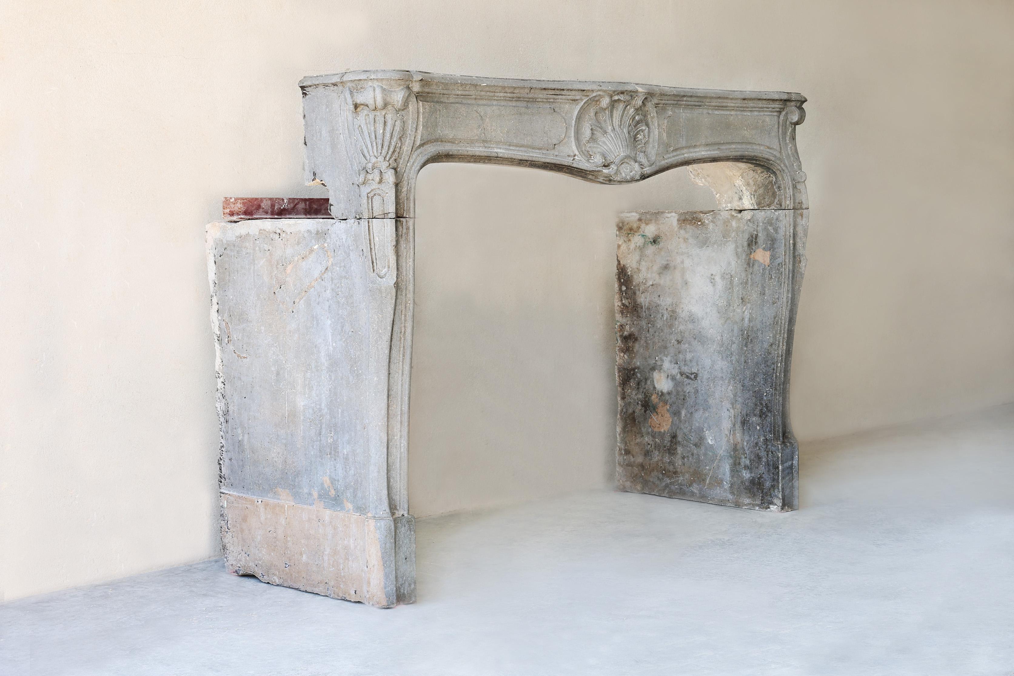 Cette belle cheminée du XIXe siècle est un chef-d'œuvre de l'élégant style Louis XV. Réalisé en pierre marbrière grise, il dégage une classe et un raffinement intemporels. Les lignes gracieuses, les formes courbes et le motif de coquillage sculpté à