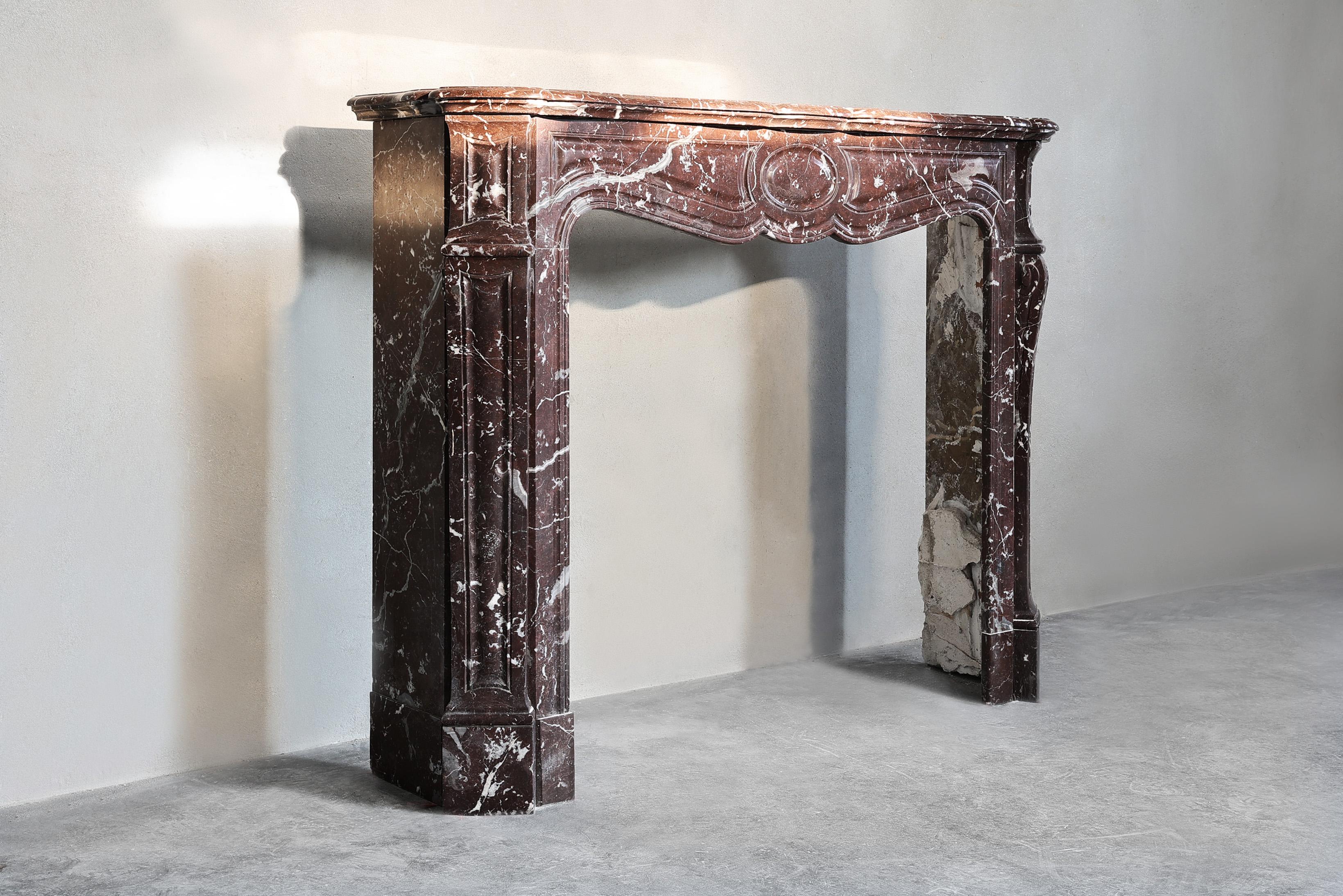 Beautiful compact mantelpiece made of Griotte Rouge marble! This antique fireplace is in Pompadour style and has a nice warm appearance. This compact model is elegant and has a graceful appearance.