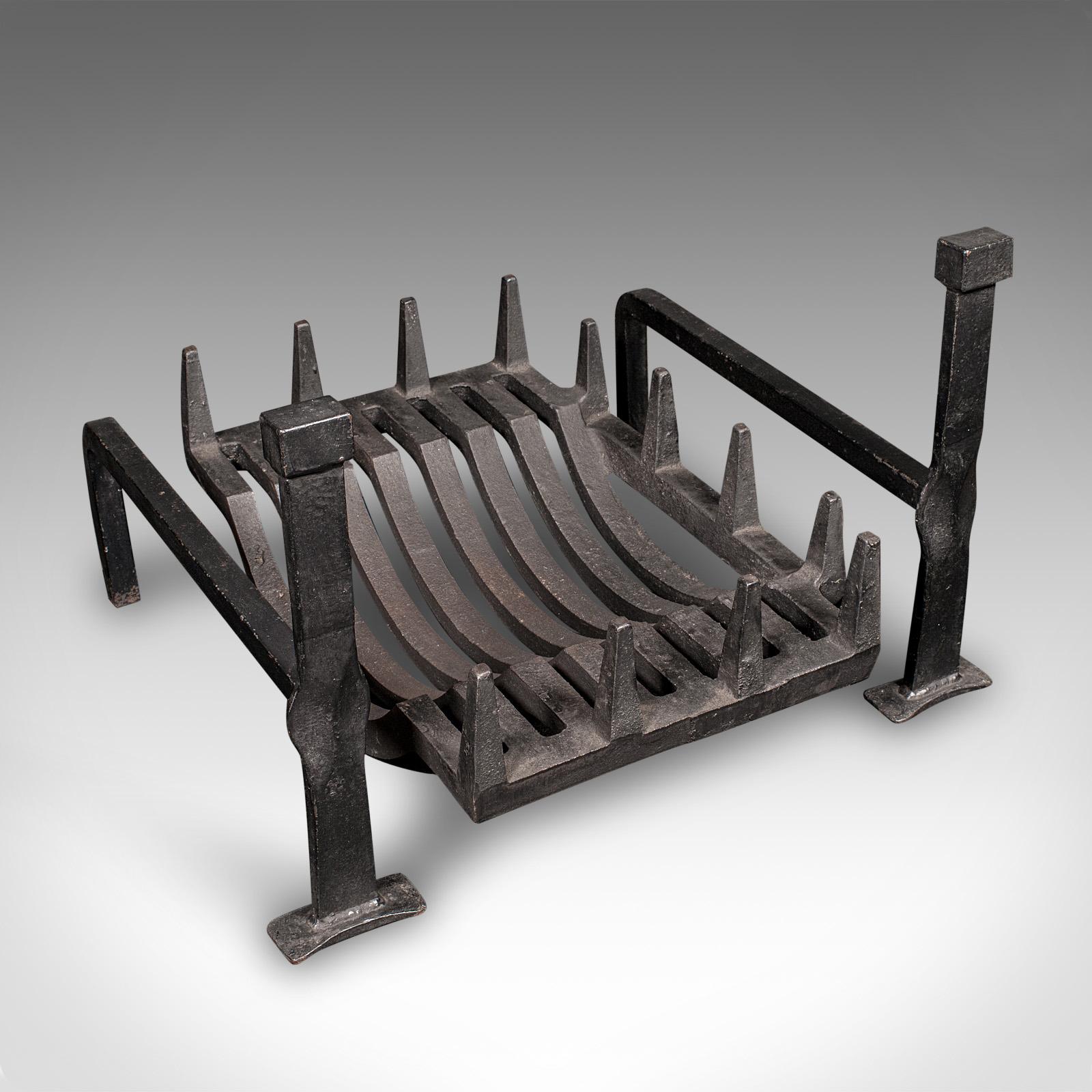 This is a charming antique fireplace set, comprising an English iron fire basket and a pair of andirons, dating to the Edwardian period, circa 1910. Offering timeless appeal and traditional craftsmanship, this ensemble is well-suited to both country