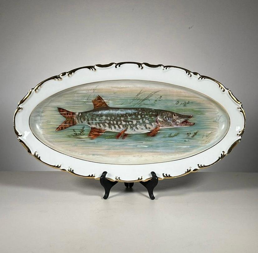 A complete Fish Service for 12 featuring a very large platter, 12 plates and an unique figural eagle handled sauce boat with a medallion of fish on each side. A slightly scalloped  wave shape to the pieces is trimmed with 24 karat gold. All fish are