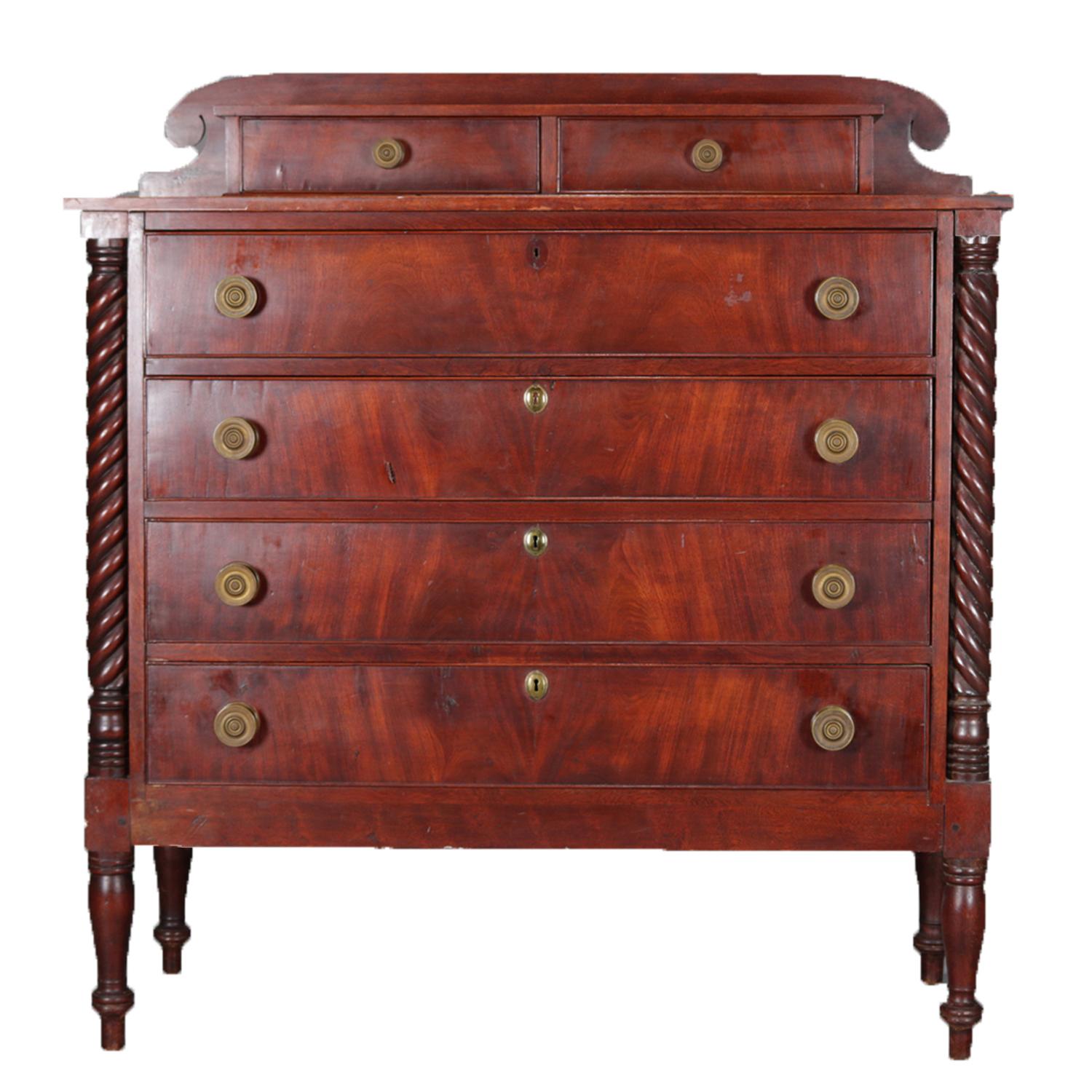 An antique Sheraton flame mahogany chest of drawers features shaped backsplash with two glove drawers over four bookmatched long drawers flanked by full rope twist columns and raised on turned feet, bronze pulls throughout, circa 1830.

Measures: