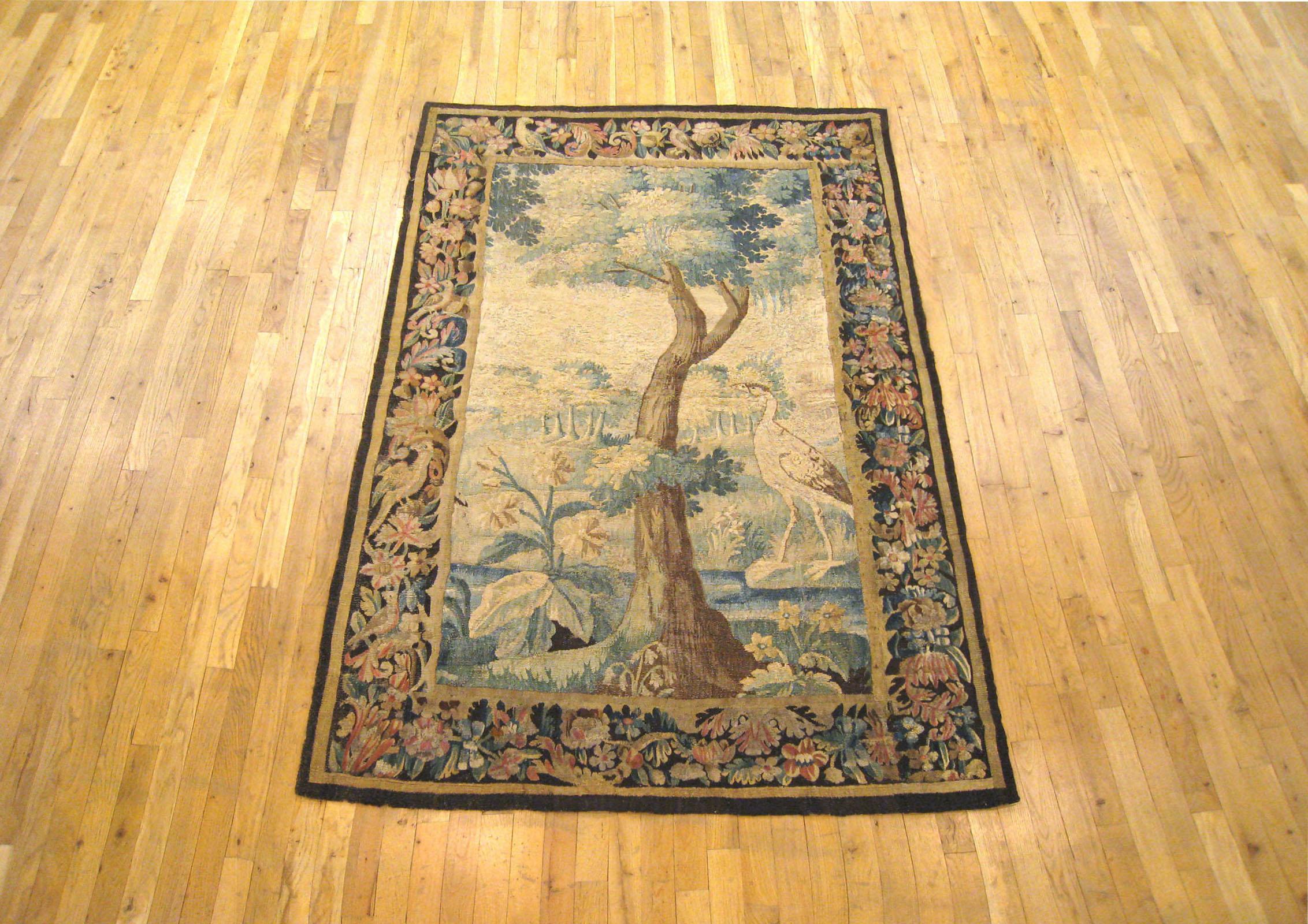 An antique Flemish verdure landscape tapestry panel from the 18th century, envisioning an idyllic setting with a stately tree and an exotic bird in the midst of verdant foliage. A tranquil scene in the tradition of the verdure tapestry, coming from