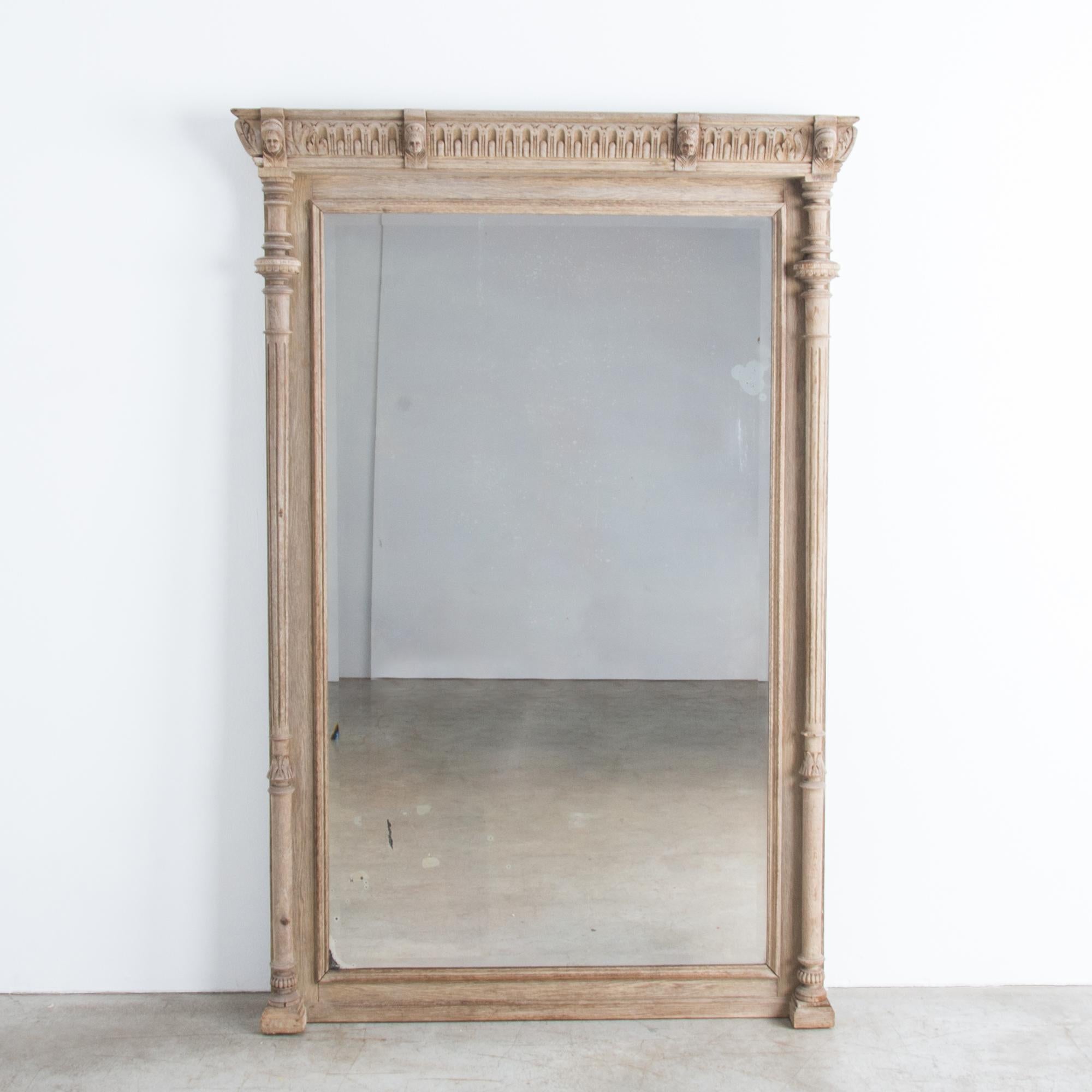 An antique floor mirror from Belgium, circa 1900, with a handsomely carved wooden frame. Slender fluted columns support an ornate lintel, featuring a repeating ornamental motif punctuated by four corbels from which emerge beautifully detailed carved