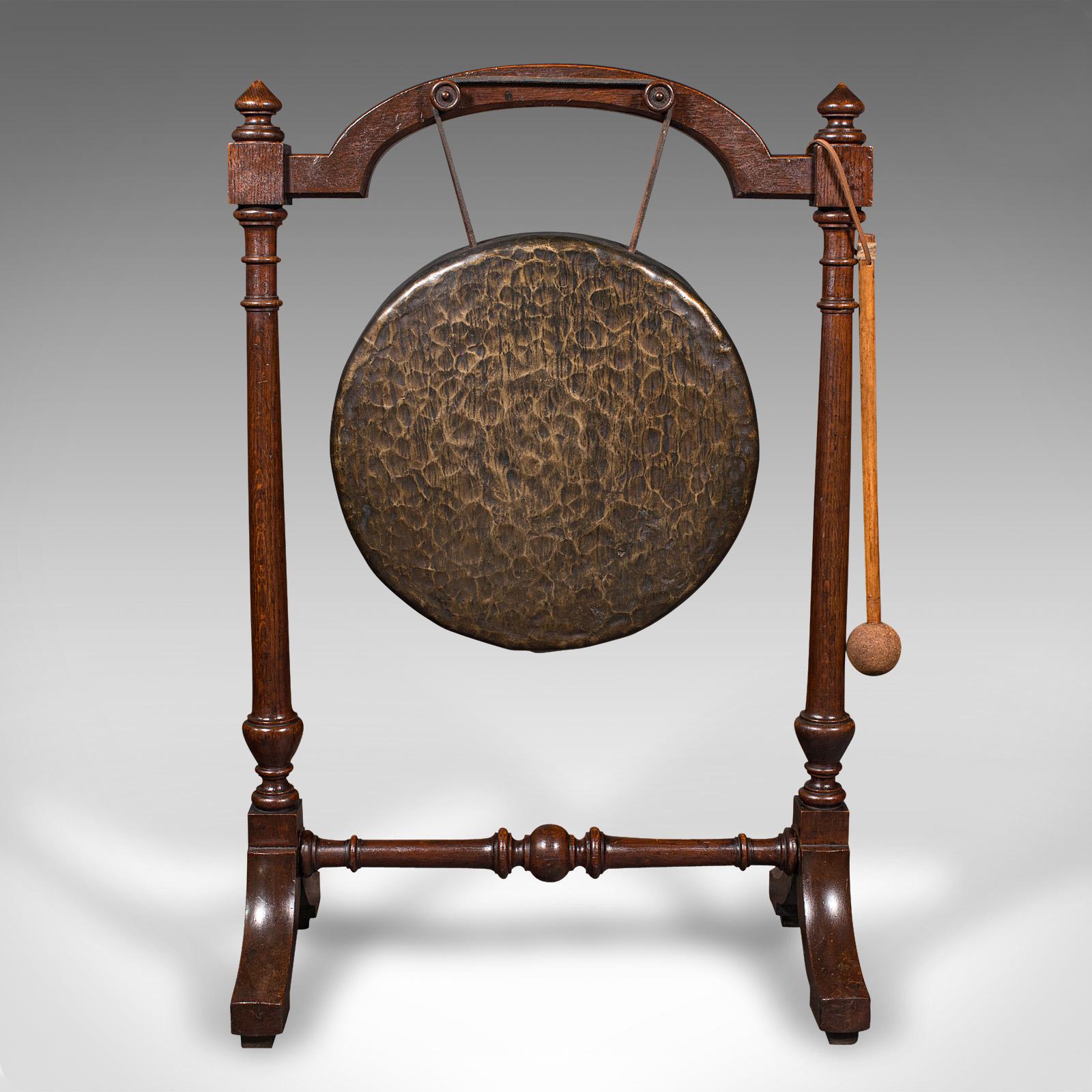 This is a large antique floorstanding dinner gong. An English, oak frame with stout bronze ceremonial cymbal, dating to the late Victorian period, circa 1880.

Of generous proportion and decorative appeal
Displaying a desirable aged patina and in
