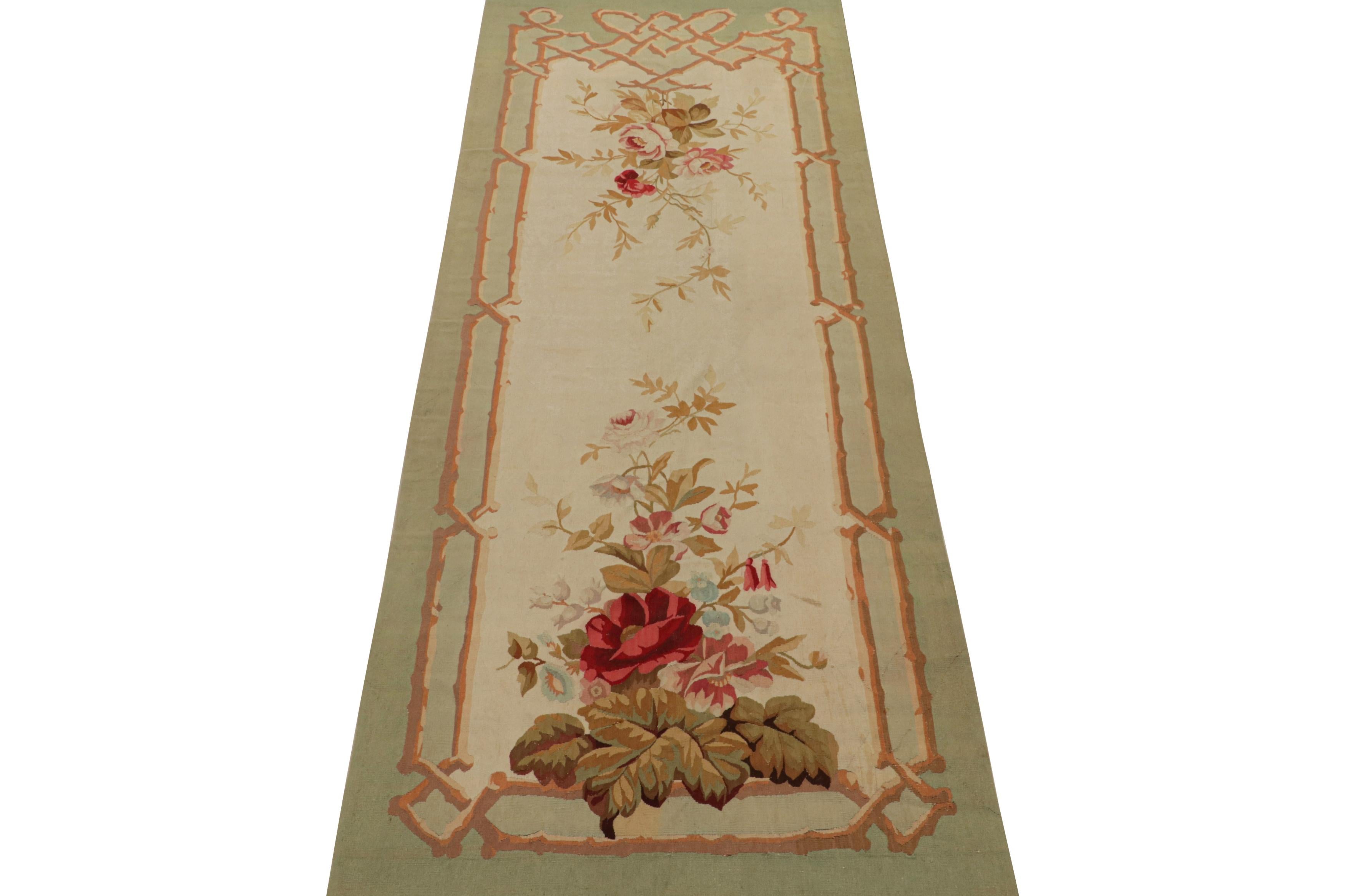 This 4x11 antique Aubusson tapestry runner rug is one of a rare set of twin flatweaves from turn-of-the-century France. Both handwoven in wool circa 1890-1900, their design features green and brown borders around a cream field with colorful, finely