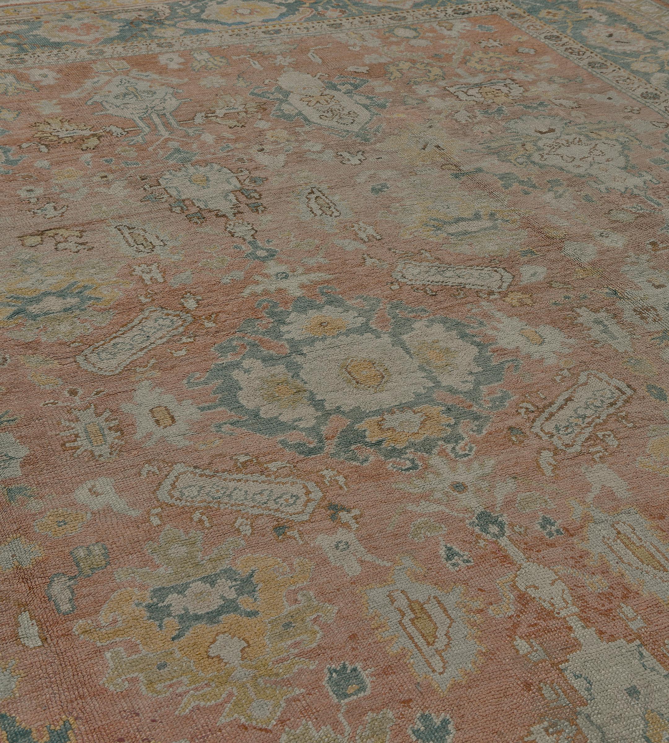 Dieser antike Oushak-Teppich zeigt ein ziegelrotes Feld mit einer zentralen, schattierten, blauen Palmette mit Palmettenanhängern, umgeben von einem kreisförmigen Band ähnlicher, hakenbesetzter, polychromer Palmetten, flankiert von eckigen, floralen