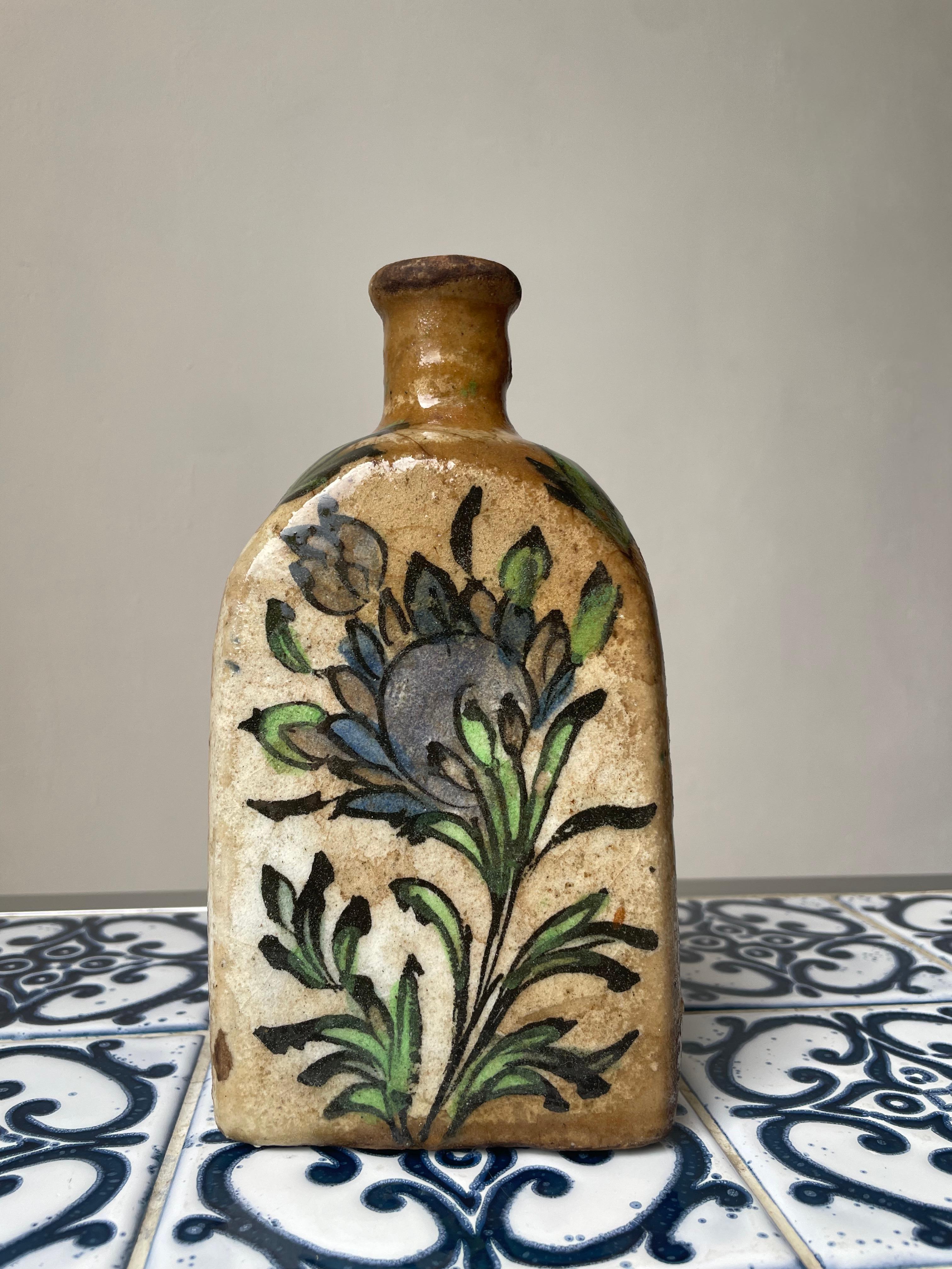 Antique handmade Middle Eastern triangular ceramic tea bottle with hand painted colorful decor and clear glaze. Green and blue colored organic floral decorations on a sand colored base with clear glaze. Manufactured in the era of the Qajar dynasty.
