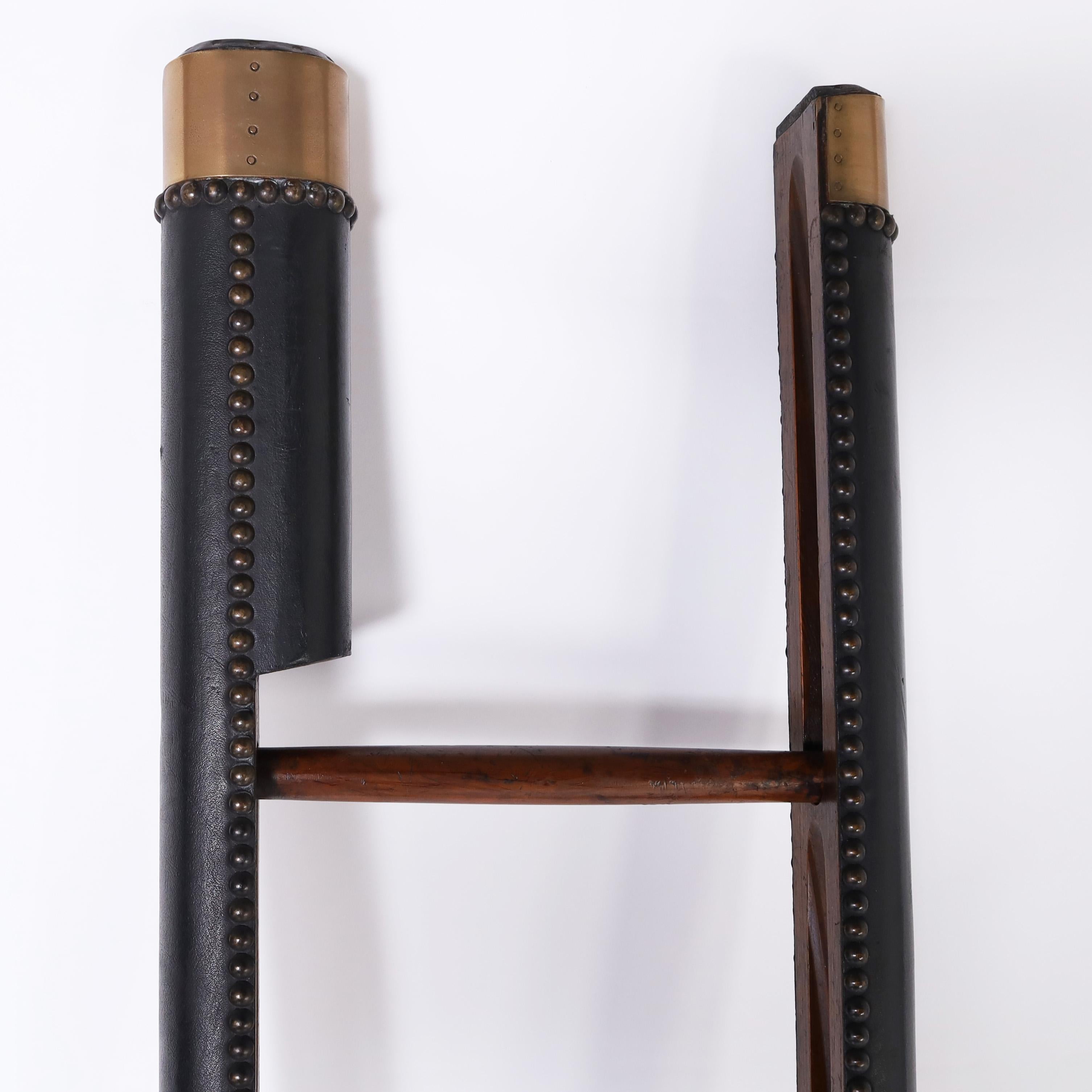 Impressive decorative English library ladder crafted in hardwoods with an ingenious folding mechanism and featuring leather covering with brass tacks, caps and feet. 

Folded dimensions H: 103 W: 3.5 D: 3