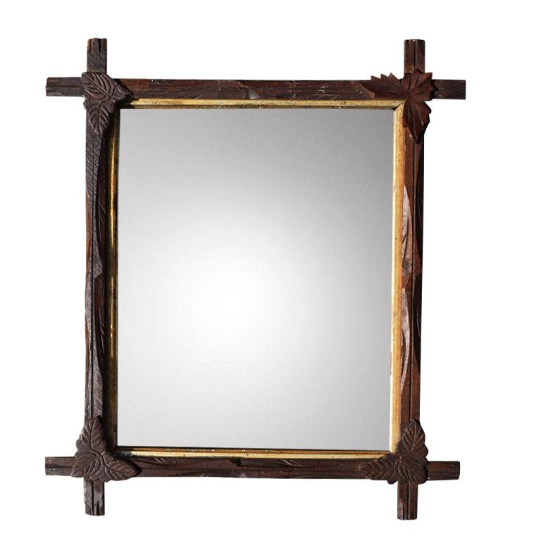 Antique and hand-carved in a dark brown wood, this tramp art style mirror is sure to make a statement in any space. At the joints, each side overlaps in a cross or Adirondack style. Carved marquetry leaves sit upon each joint. The interior of the