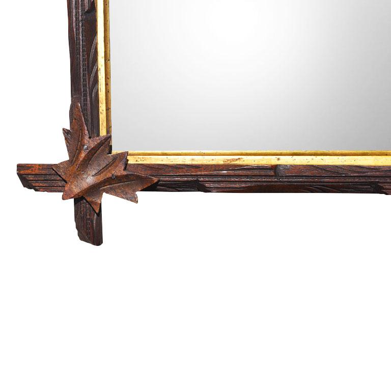 Antique hand-carved in a dark brown wood, this tramp art style mirror is sure to make a statement in any space. At the joints, each side overlaps in a cross or Adirondack style. Carved leaves sit upon each joint. The interior of the mirror is