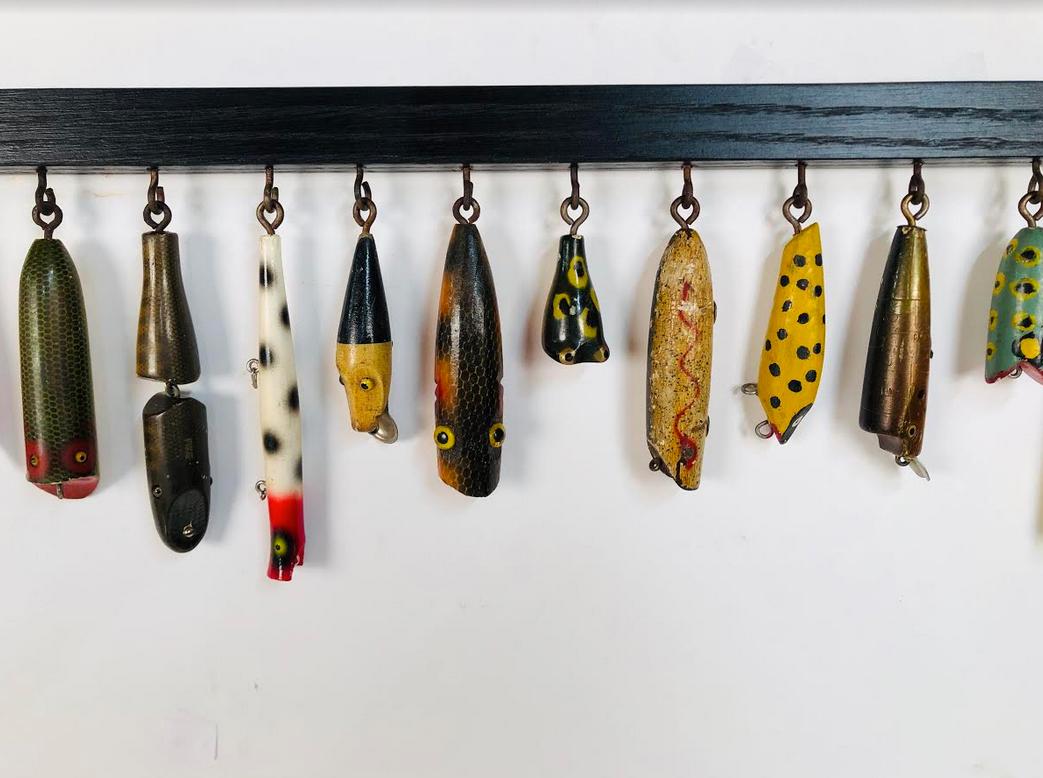 A collection of 30 antique and vintage wooden fishing lures displayed on a black painted oak display with acid ages eye hooks. Mounted on a black paint oak display with acid aged hook eyes.