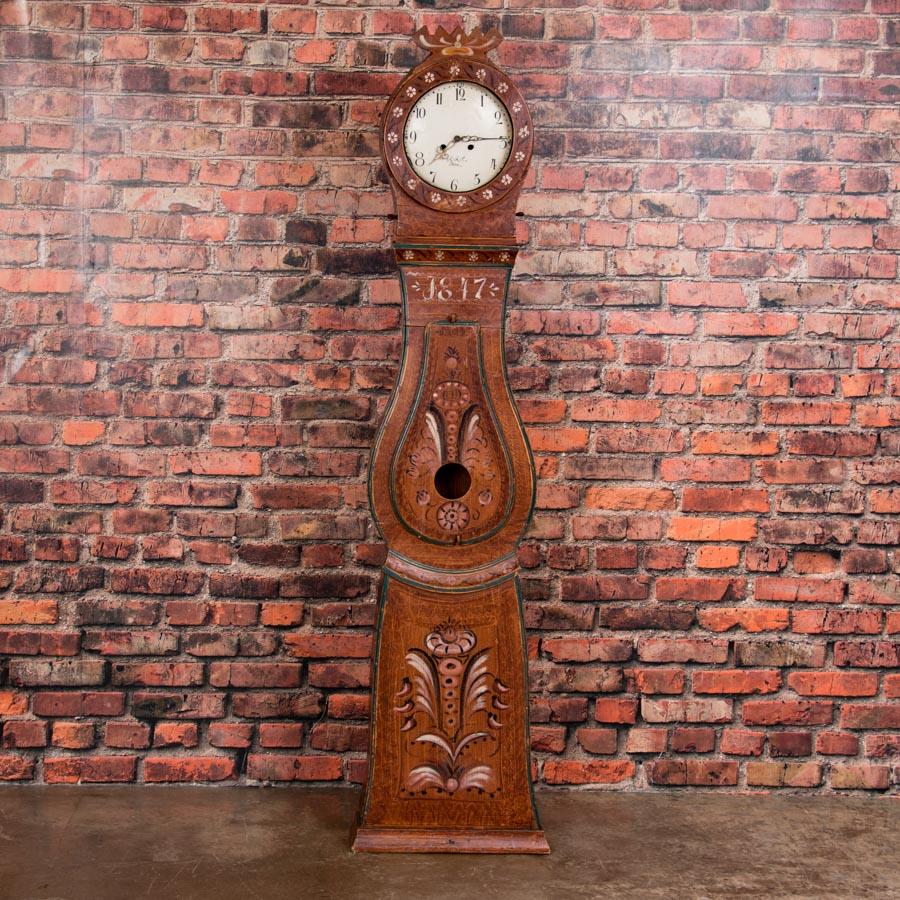 A traditional antique Swedish Mora clock dated 1847 retaining the original folk art paint, mostly earth tones of brown and terra cotta. This lovely clock, not too tall, with great proportions and visual appeal, stands at just over 6 1/2 feet