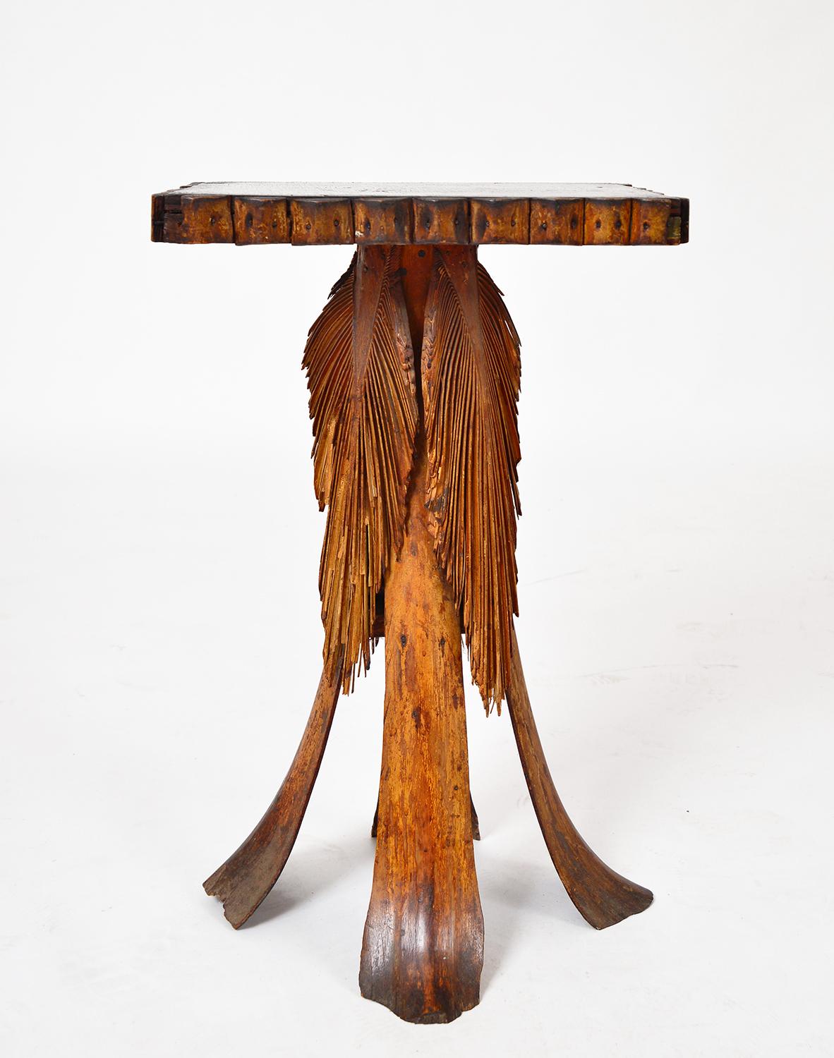 A stunning example of a Folk Art palm frond accent table dating from the early 20th century. The four legs are large palm fronds, flanked by beautiful decorative palm leaves. The top has a decorative tramp art style palm apron and a nicely worn