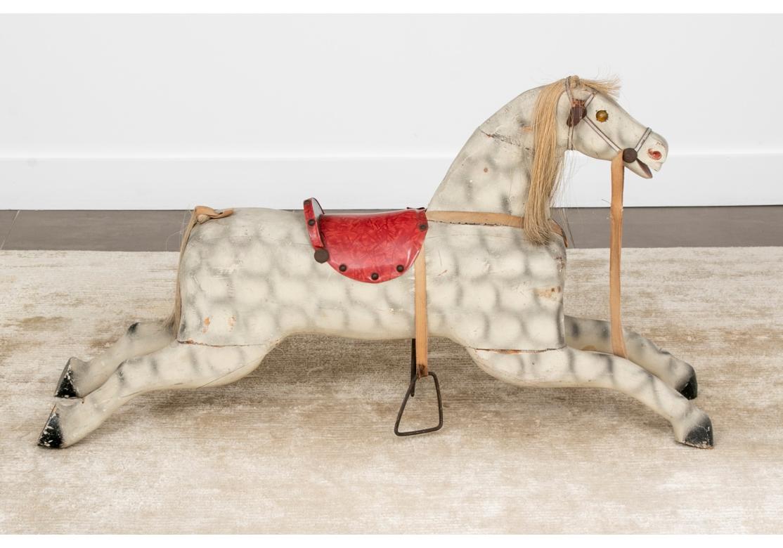 Une vibrante sculpture de cheval à bascule d'art populaire antique en  état d'origine. Le cheval a une belle forme primitive, de belles enjambées, des yeux à facettes, des étriers en fer, une selle en vinyle rouge avec des garnitures en tête de clou