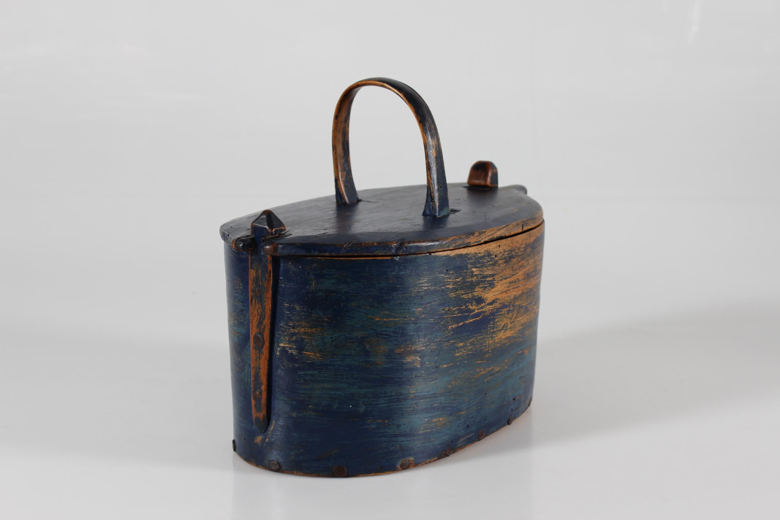Antique Scandinavian wooden container with original dark blue paint which is worn off at places. The side are made of one single piece of wide bent wood, closed will stiches of natural material. 
The bottom of the box and the top of the lid are of