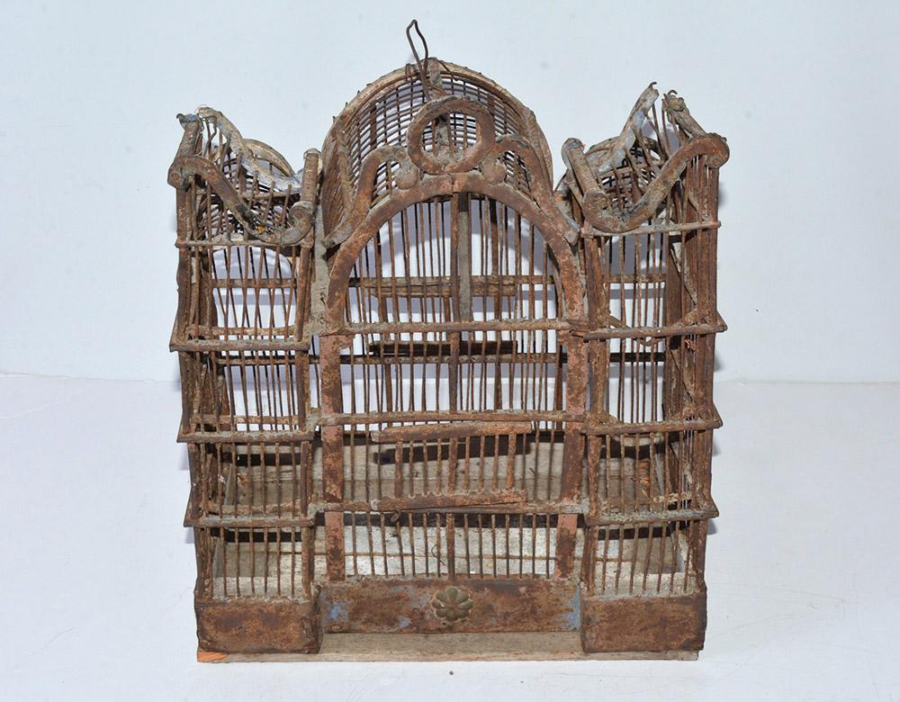 The antique bird house is composed of wire and wood framing and floor. The front facade has an arched center section and side 