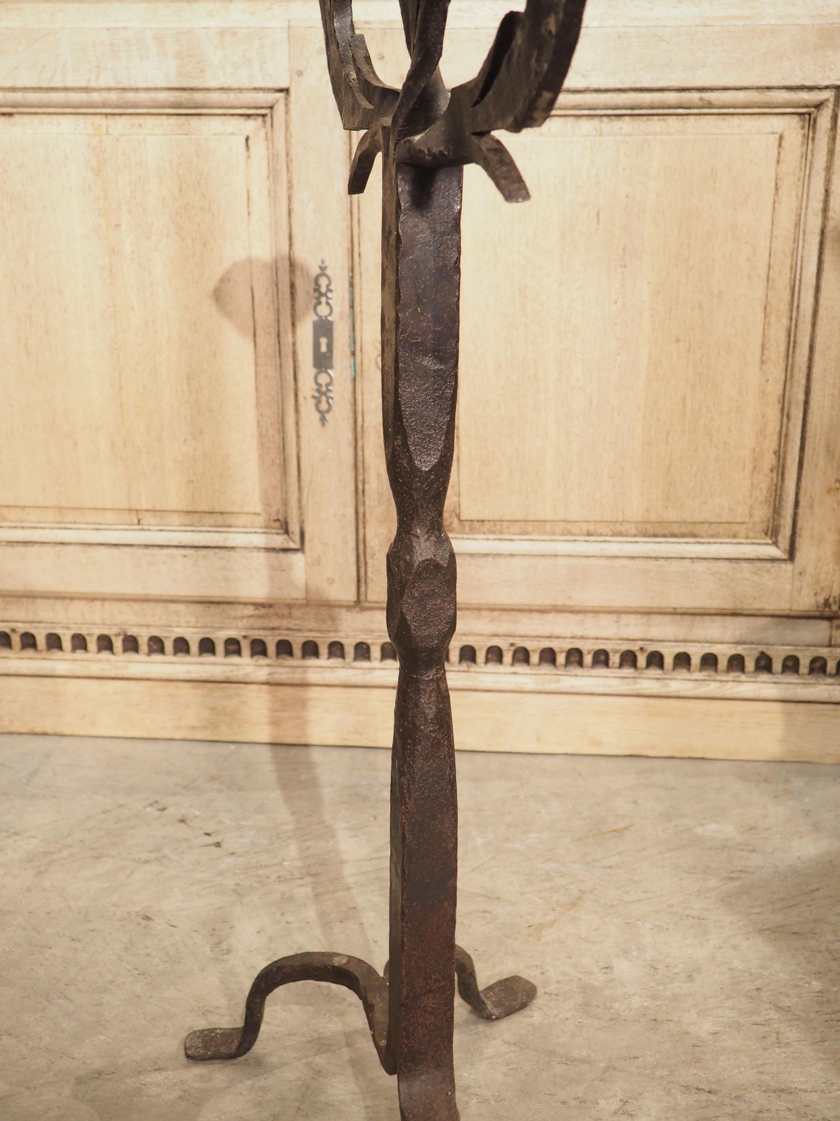 Forged in Spain, circa 1900, this iron candelabra torchere has three arms embellished with angular protrusions, in the form of stylized leaves emanating from a plant stem. Each arm is topped with undulating circular bobeches and a geometric pricket,