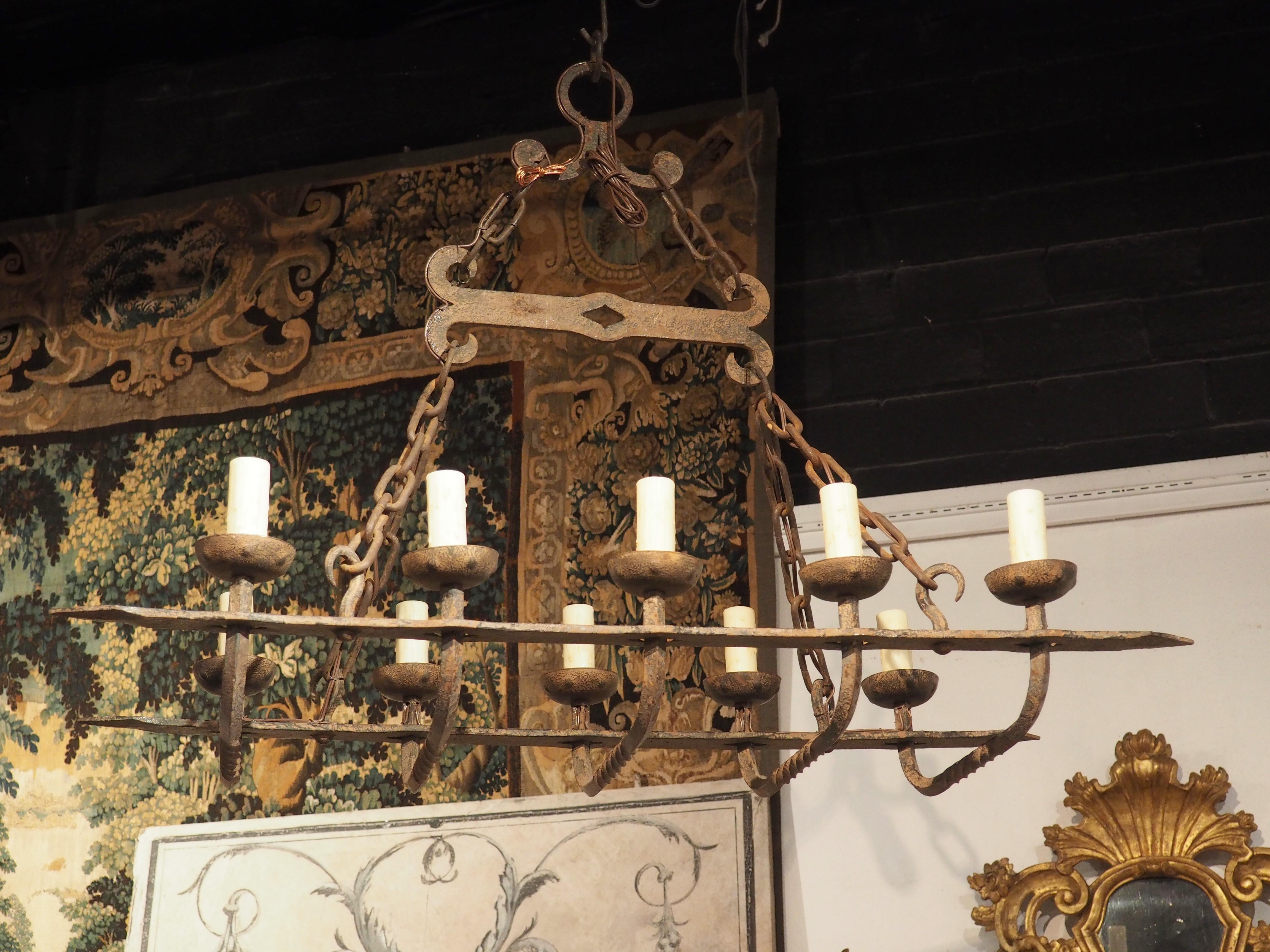This rustic antique French ten light iron chandelier has been hand forged into a rectangular shape. There are five square iron rods turned diagonally with twist turned motifs at the bottom center. At the ends of these rods and curving upwards