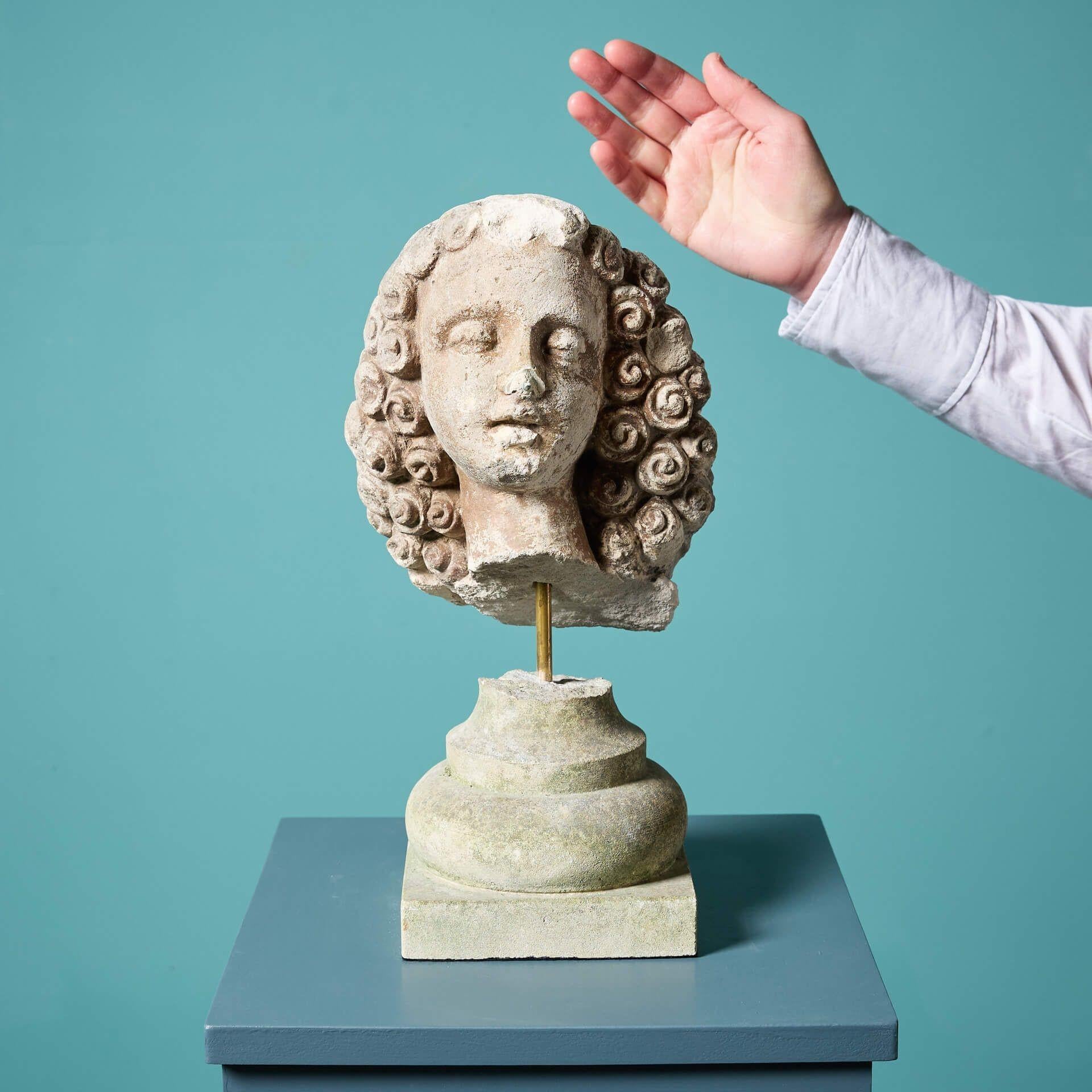An antique fragmentary carved stone head circa 1800, mounted on an associated limestone socle base with brass stem.
 
Once part of a larger limestone statue, this fragment has survived the test of time with details of the figure’s head still intact