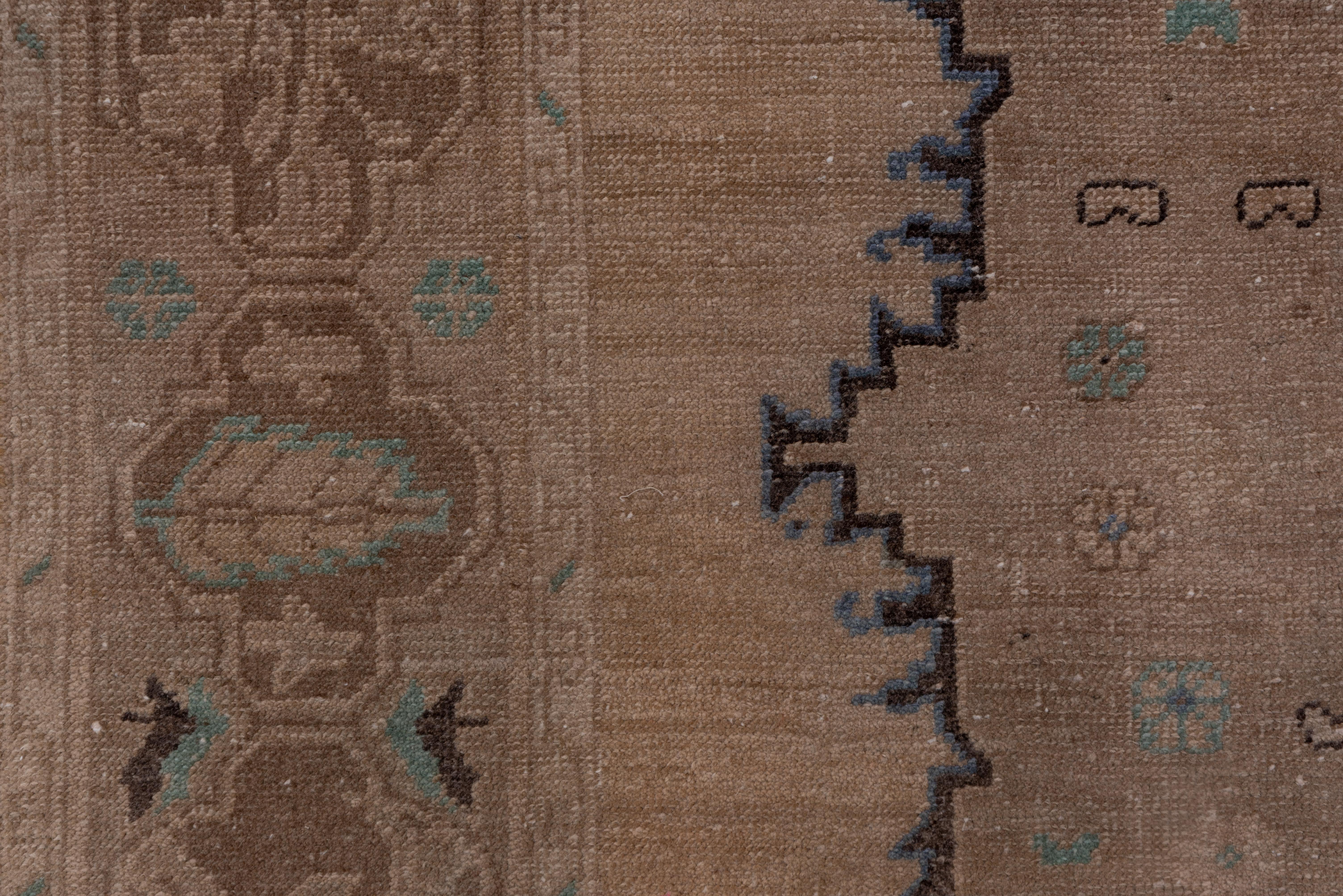 With a peach cypress and bud border on three sides only, this Turkish village rug features a very light brown open field with a central pole medallion of three flattened octogramme cartouches fitted within triangular corners defined by broad dark