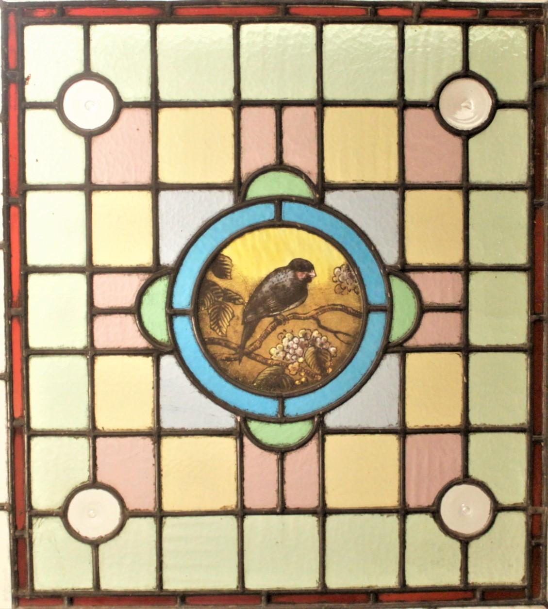 This very elaborate antique stained glass window was likely made in the United States in circa 1880 in the period Victorian style. This stained glass panel features a hand-painted bird in the central circular medallion. The window is done in muted