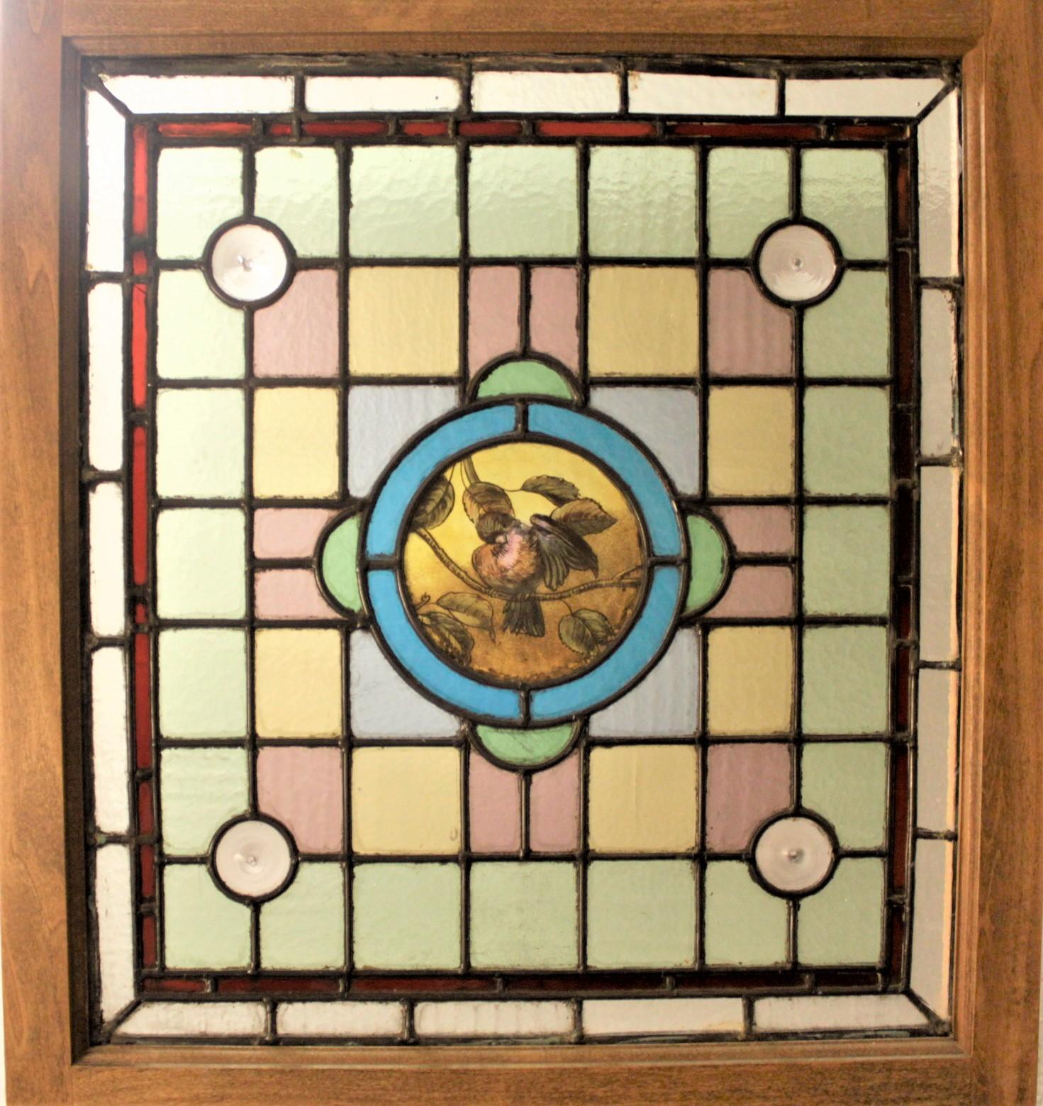 This very elaborate antique stained glass window was likely made in the United States in circa 1880 in the period Victorian style. This stained glass panel features a hand painted bird in the central circular medallion. The window is done in muted