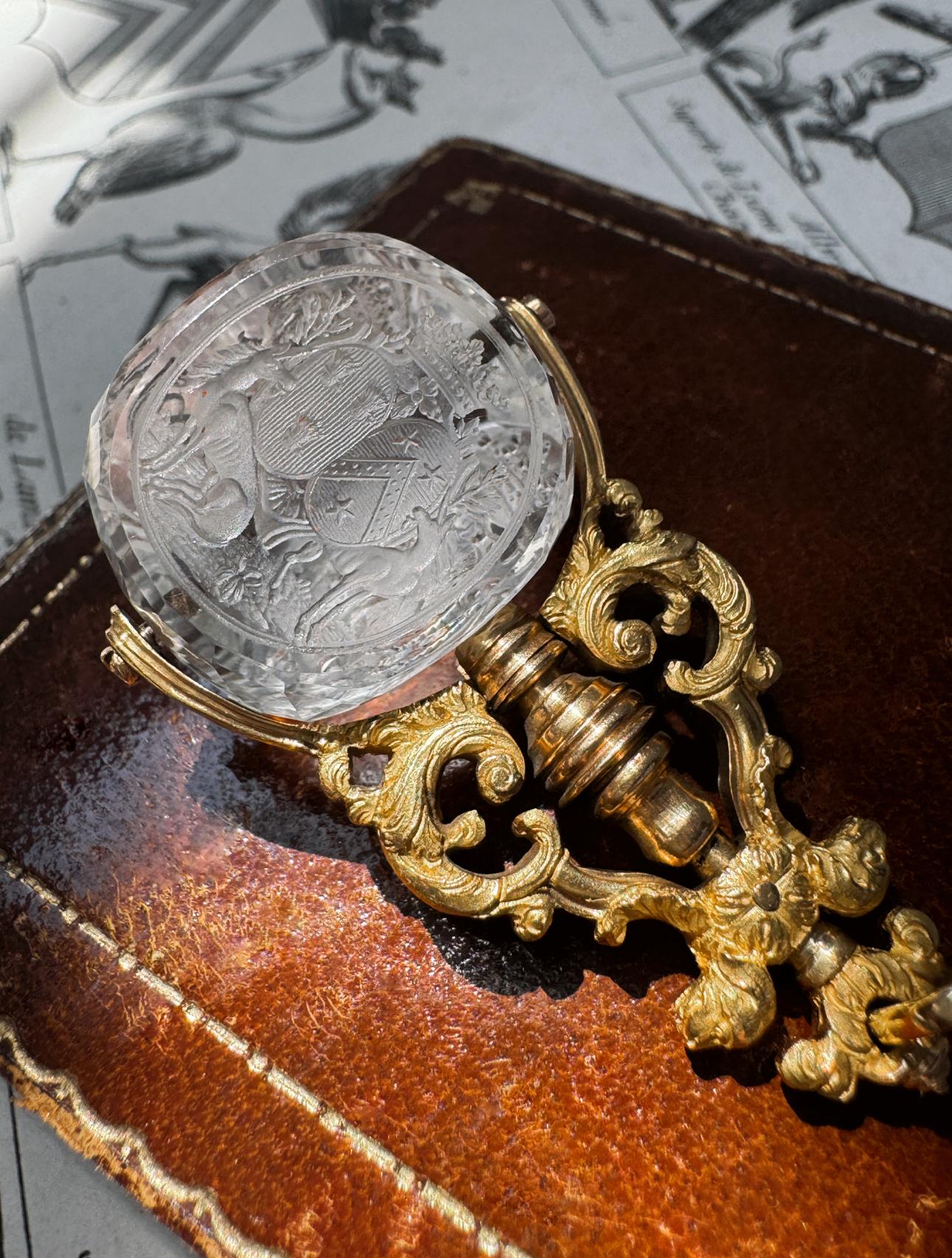 Dating to early 19th century France, this exquisite rock crystal fob has been hand fabricated in 18 karat gold. The ornate handle features a pair of loyal dogs flanking a scrolling openwork design which supports a revolving triple sided rock crystal