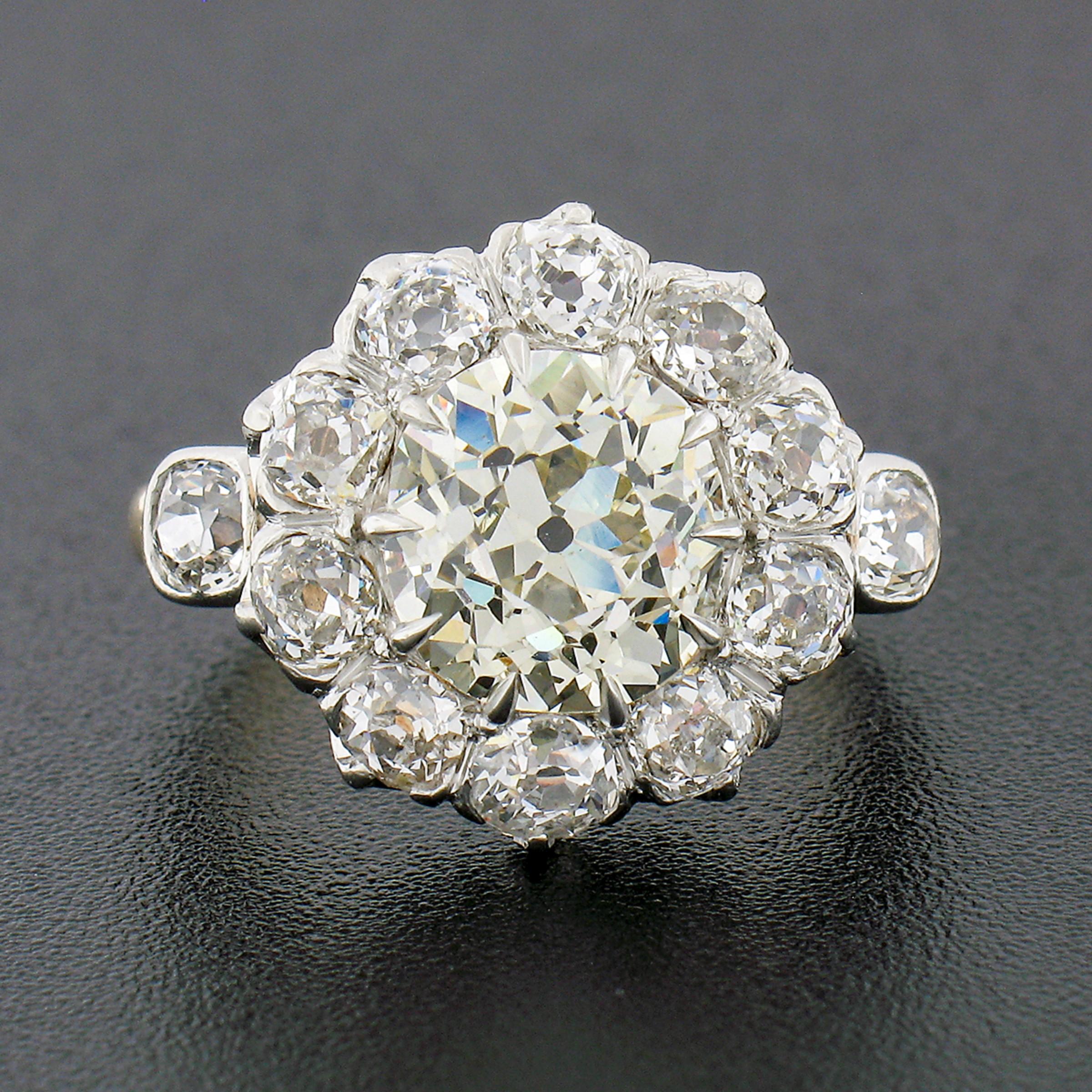 This stunning, handmade, antique flower cluster ring was crafted from solid 18k yellow gold with a platinum top during the Edwardian period. It features a breathtaking, old mine cut diamond neatly multi-prong set at the center, displaying a super