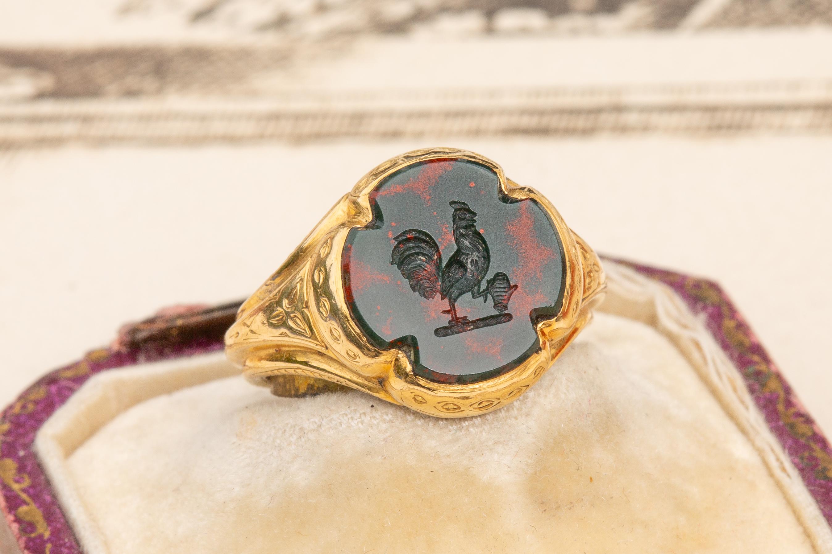 A superb antique signet seal ring dating to the second half of the 19th century, circa 1870. In the centre, a flat bloodstone of a cross shape has been intricately carved to depict an unusual coat of arms with a heraldic Gallic rooster or ‘coq