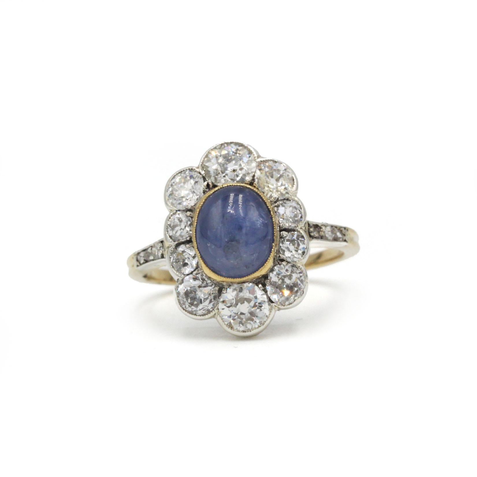 Schöner antiker französischer Ring aus 18 Karat Gelbgold mit einem zartblauen Cabochon-Saphir, der von einem schimmernden Ring aus acht Diamanten im Altschliff von insgesamt etwa 2,00 Karat umgeben ist.
Das florale Cluster-Design fängt den